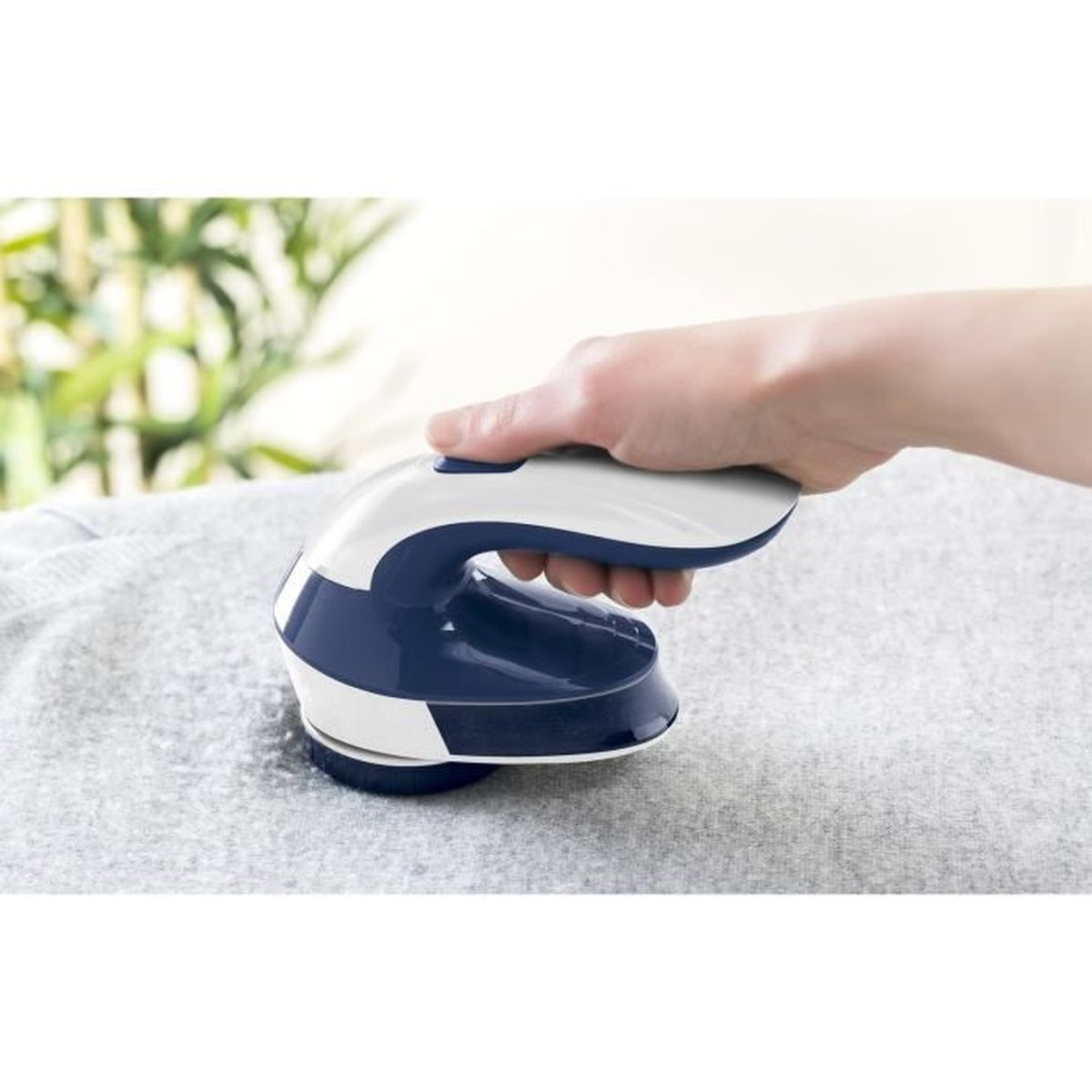 Una mano tiene un rifinitore per tessuti blu e bianco su un maglione grigio.