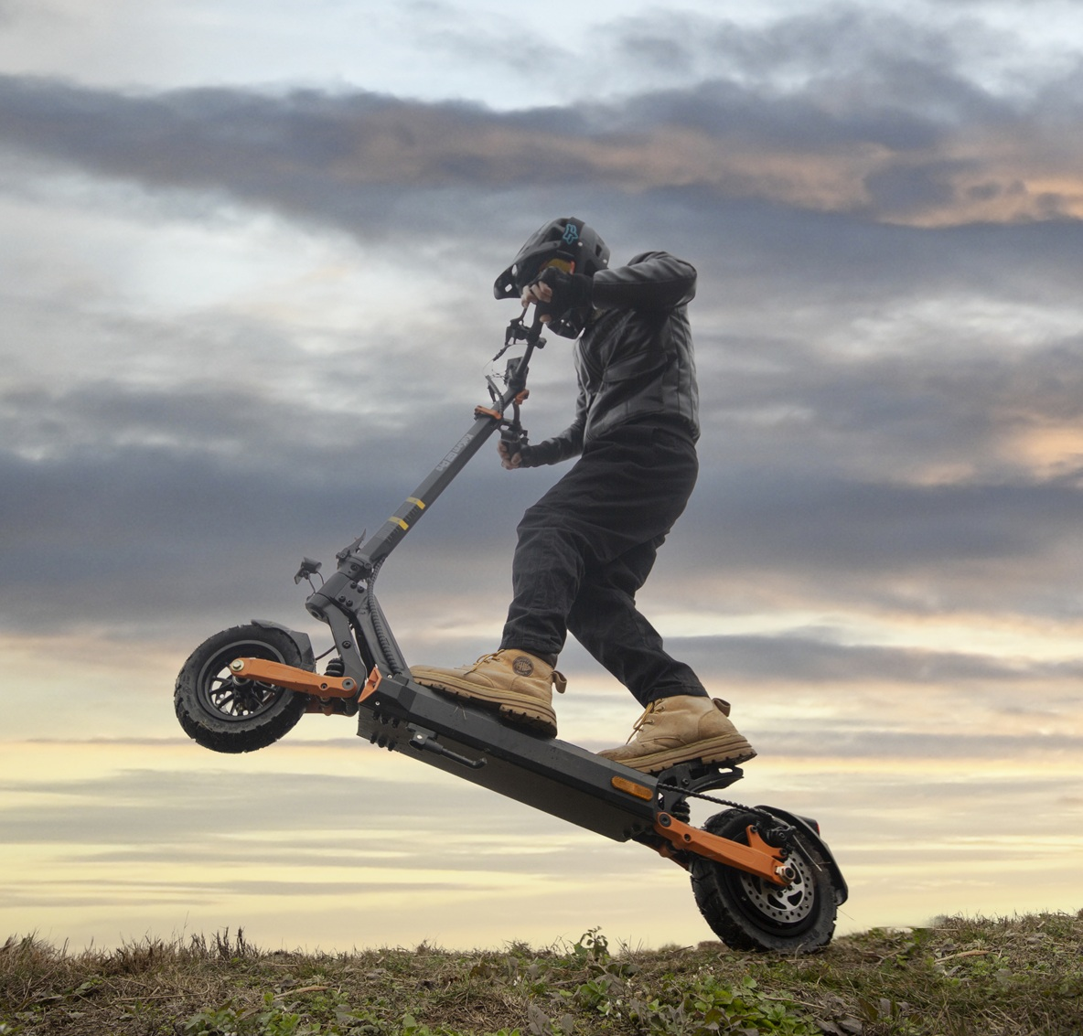 Una persona con equipo completo monta un patinete eléctrico, saltando sobre un campo.
