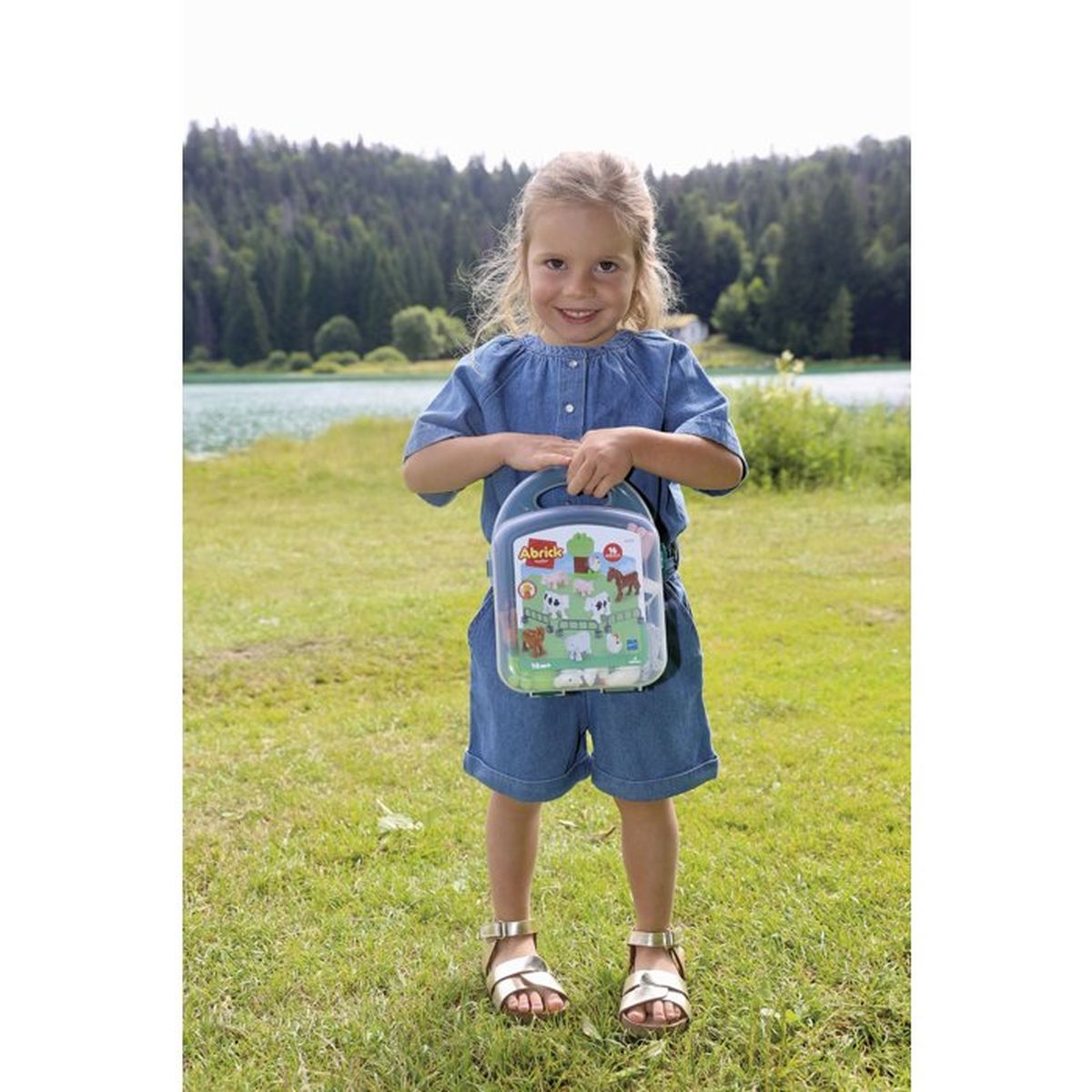 Una bambina in jeans tiene una scatola di giocattoli con animali da fattoria.