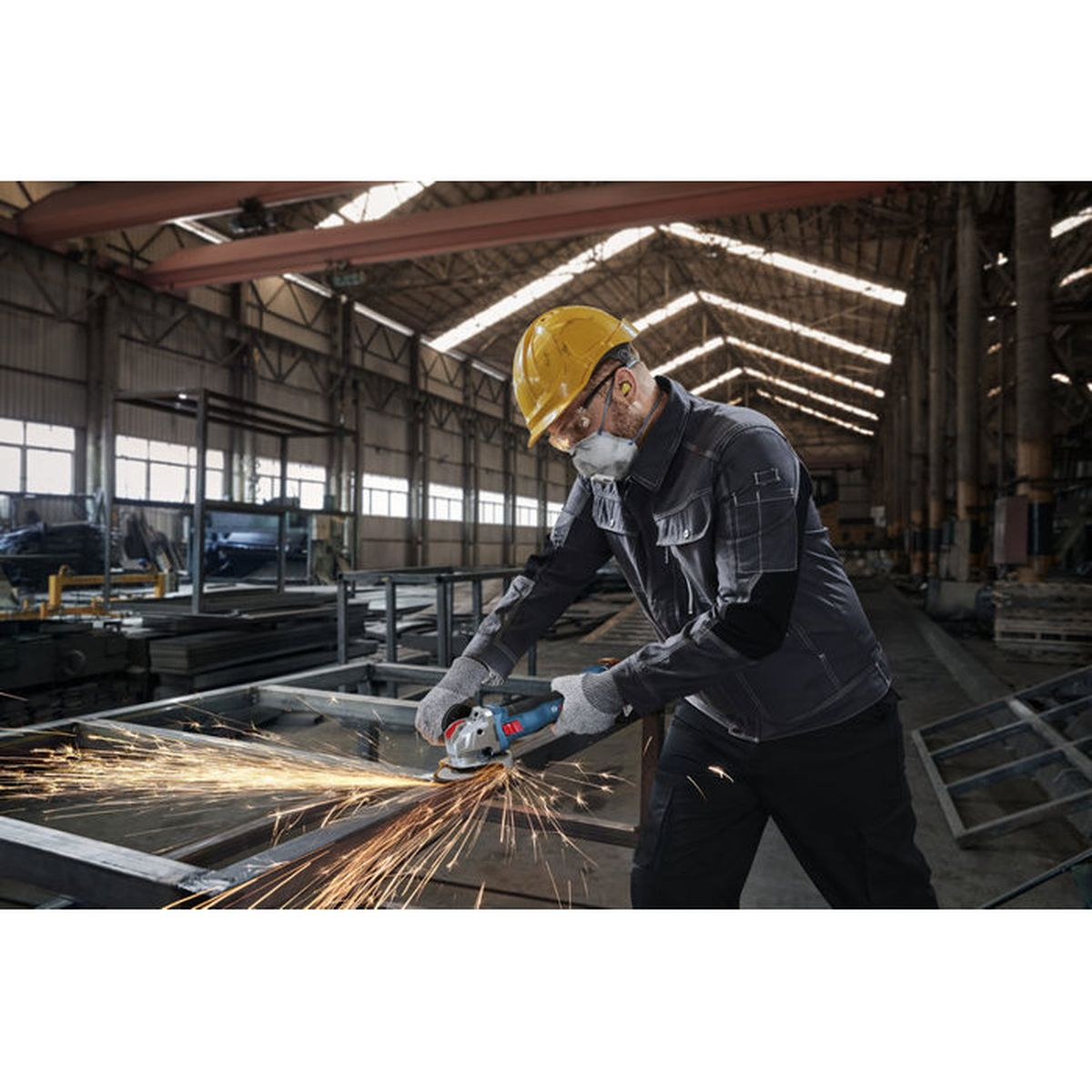 Ein Arbeiter schleift Metall in einer Fabrik, Funken fliegen.