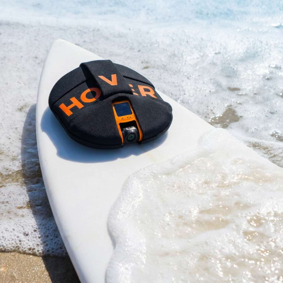 Ein schwarzer Hovercam-Schutz mit orangefarbenen Buchstaben liegt auf einem weißen Surfbrett.
