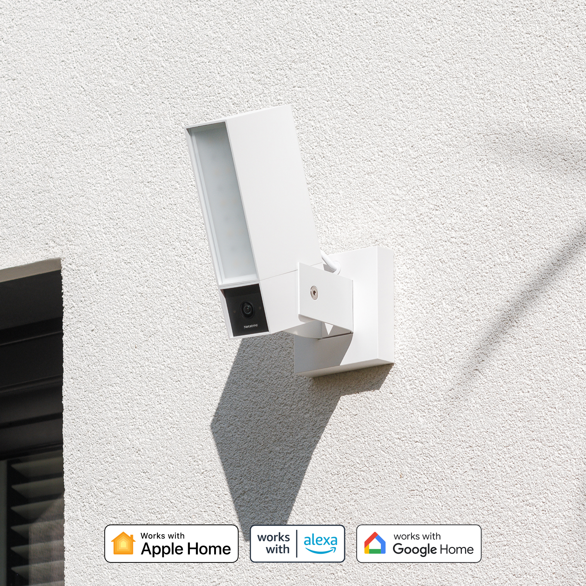 Witte camera met licht en logo's voor Apple, Alexa, Google Home op muur.