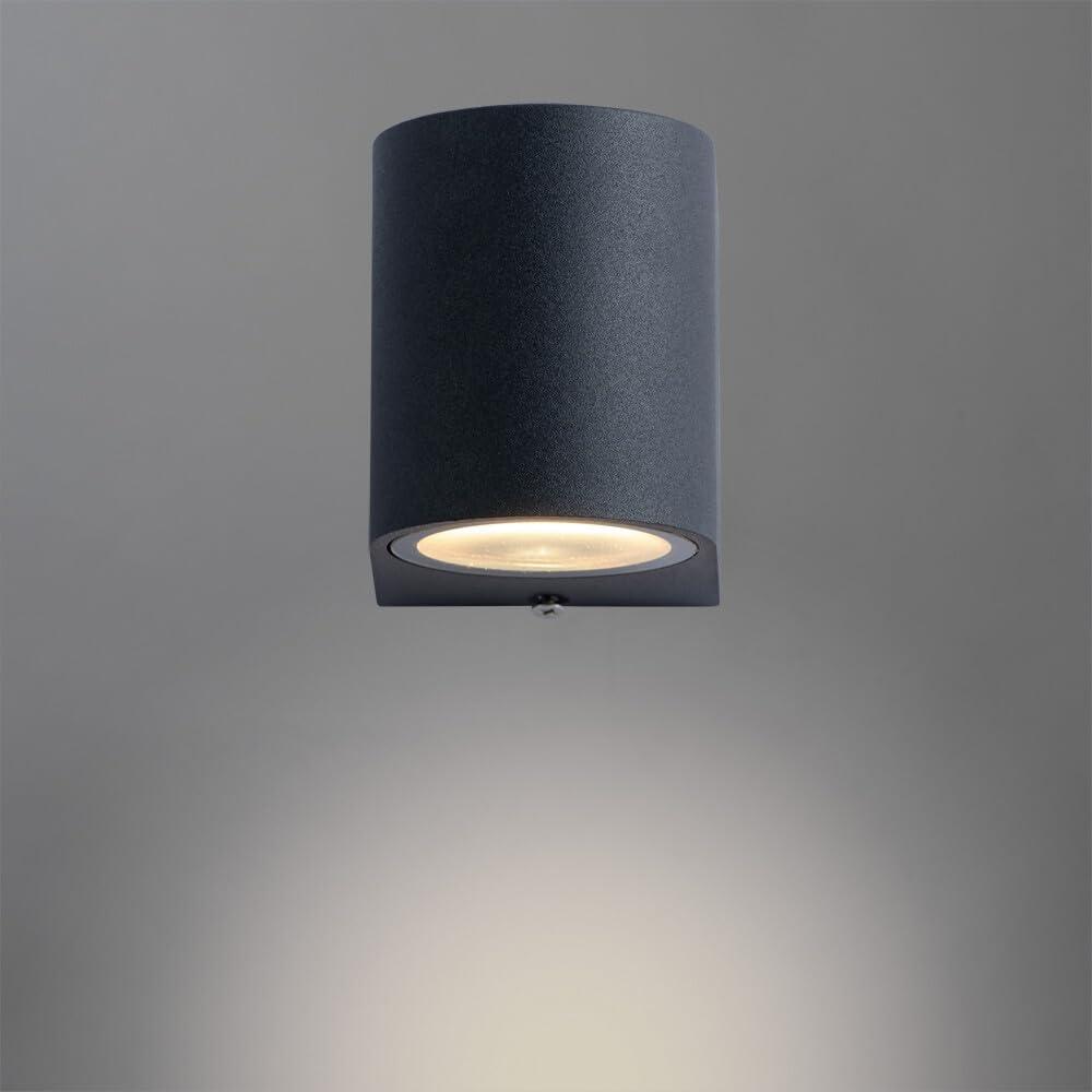 Eine dunkle, zylindrische Wandleuchte mit nach unten gerichtetem Licht auf grauem Hintergrund.