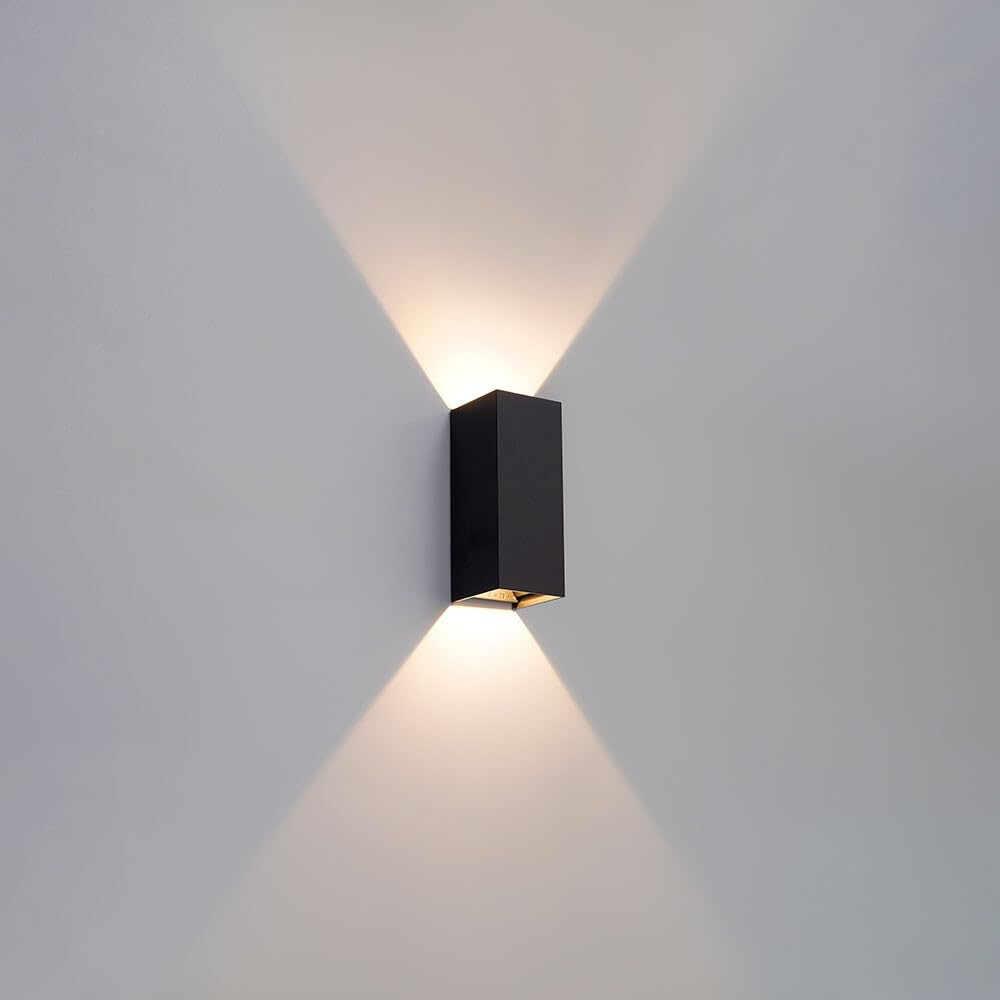 Ein schwarzer Wandleuchter leuchtet nach oben und unten auf eine weiße Wand.