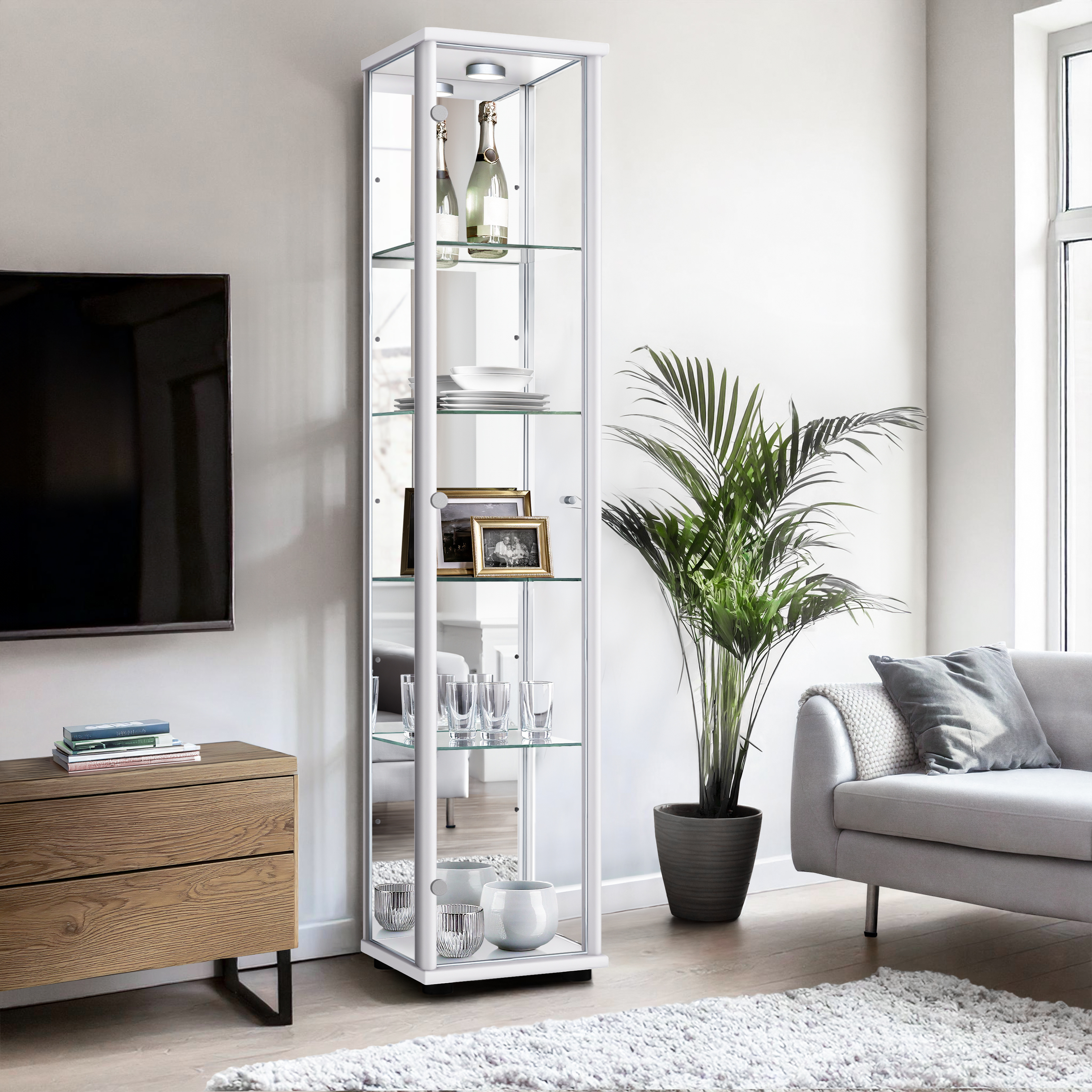 Ein schmaler Vitrinenschrank mit Glasböden steht neben einem Sofa und einem Holzbüfett.