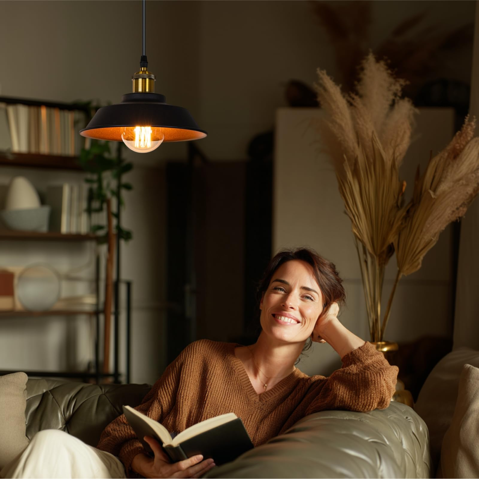 Frau liest auf Sofa. Hängelampe über ihr. Trockenblumen im Hintergrund.