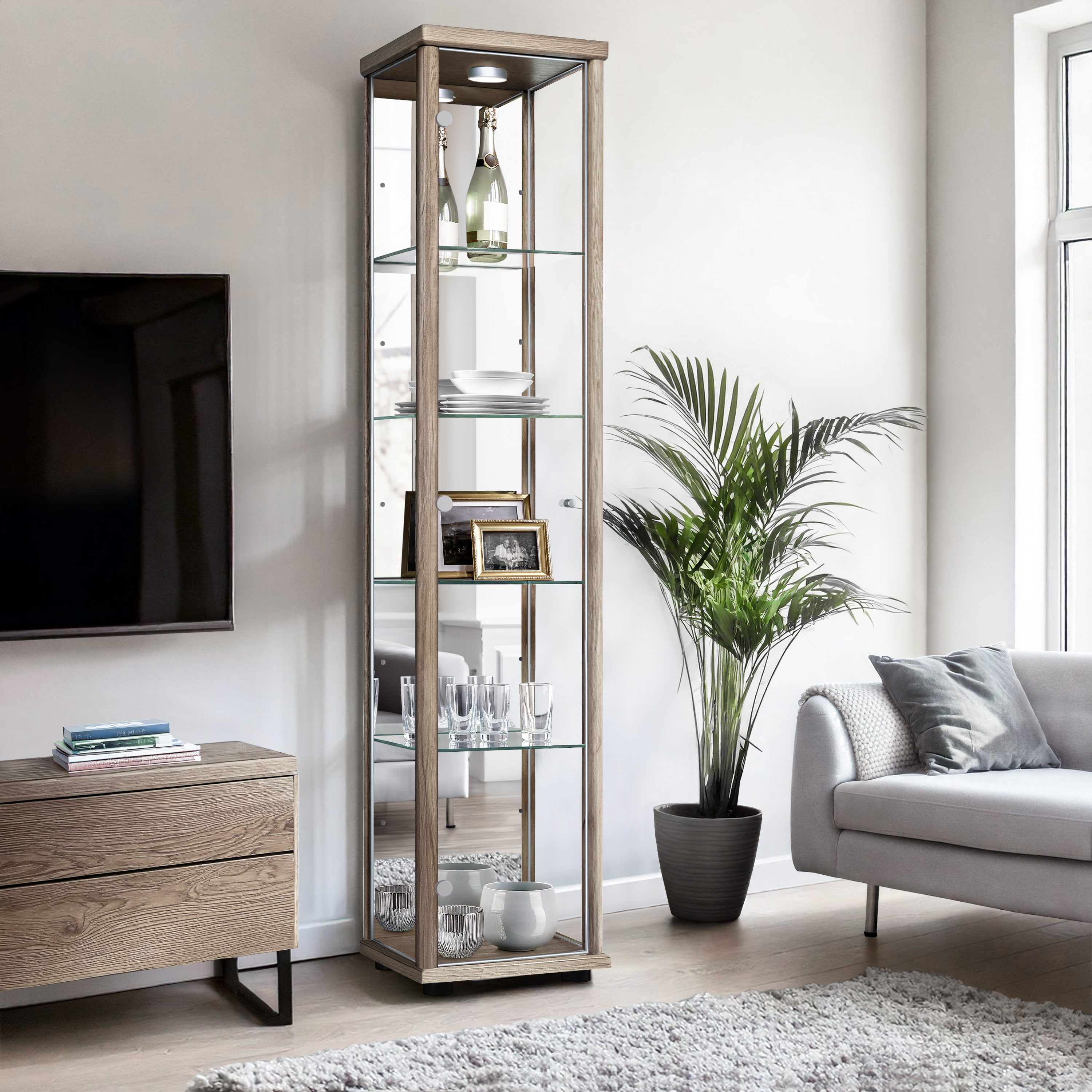Ein schmaler, beleuchteter Vitrinenschrank aus Holz und Glas steht neben einem Sofa.