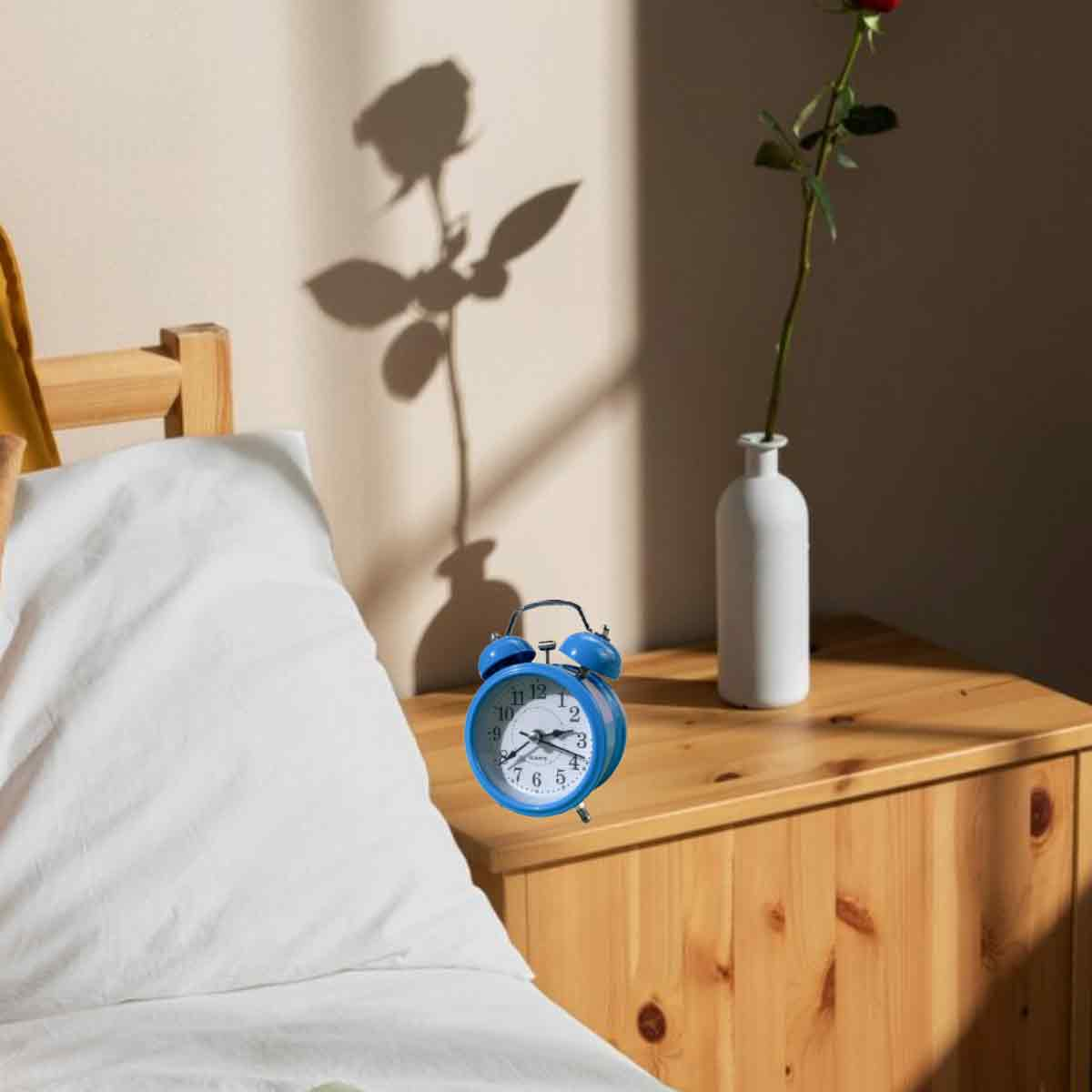 Ein blauer Wecker steht auf einem Nachttisch neben einem Bett.