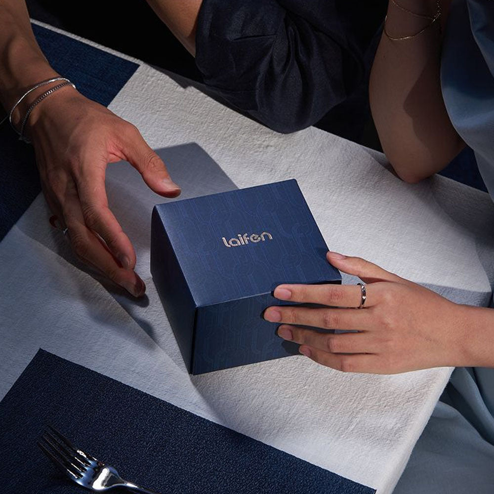 Zwei Hände halten eine blaue Schachtel mit der Aufschrift „laifen“ auf einem weißen und blauen Tuch.