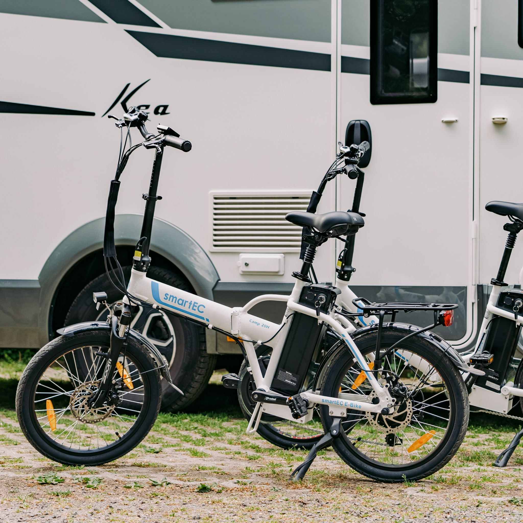 Zwei weiße Elektrofahrräder stehen vor einem Wohnmobil. Das linke Fahrrad ist vorne und das rechte teilweise sichtbar.