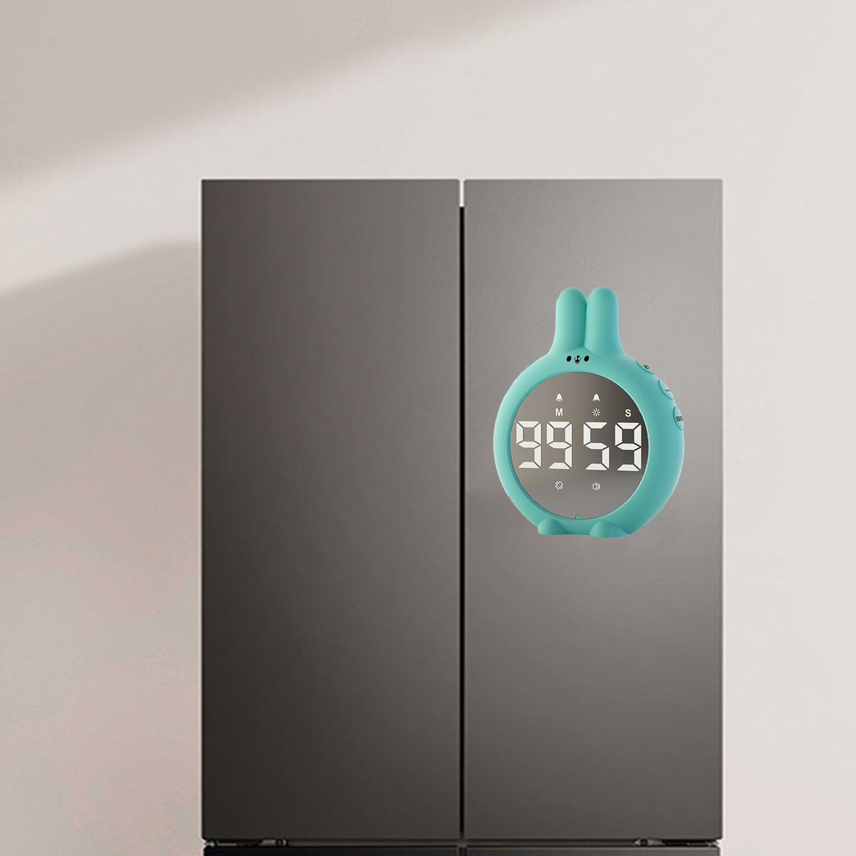 Ein türkisfarbener Hasen-Timer mit digitaler Anzeige klebt an einem grauen Kühlschrank.