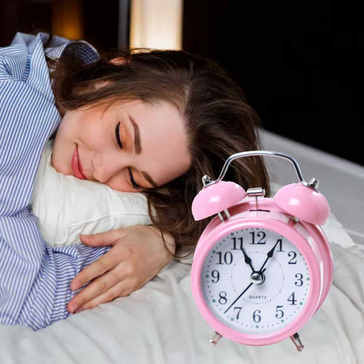 Eine Frau im gestreiften Pyjama schläft auf einem Kissen neben einem rosa Wecker.