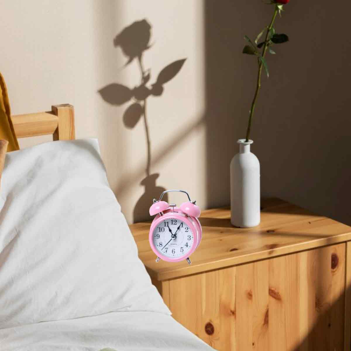 Ein rosafarbener Wecker steht auf einem Nachttisch neben einem weißen Bett.