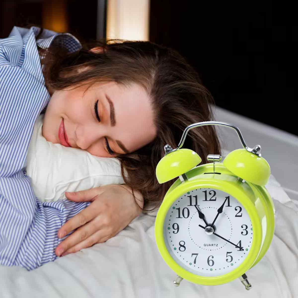Frau schläft neben einem hellgrünen Wecker auf einem weißen Bett.