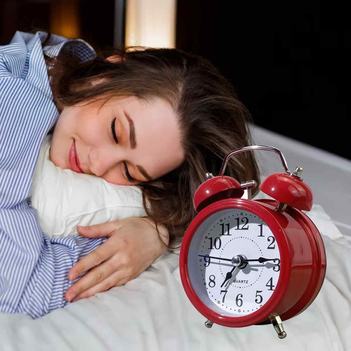 Eine Frau schläft auf einem Kissen mit einem roten Wecker auf dem Bett.