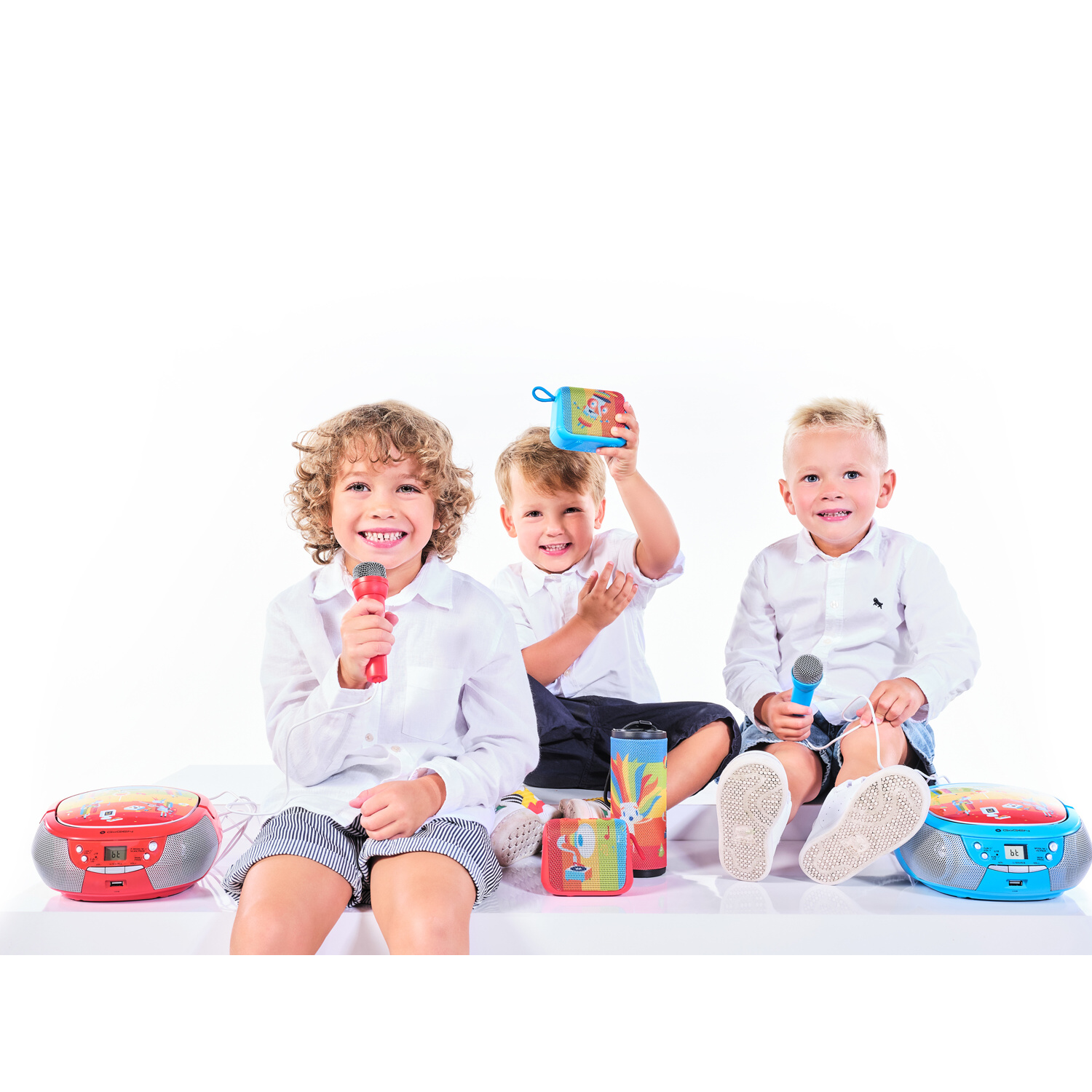 Tre bambini seduti con microfoni e lettori musicali su sfondo bianco.