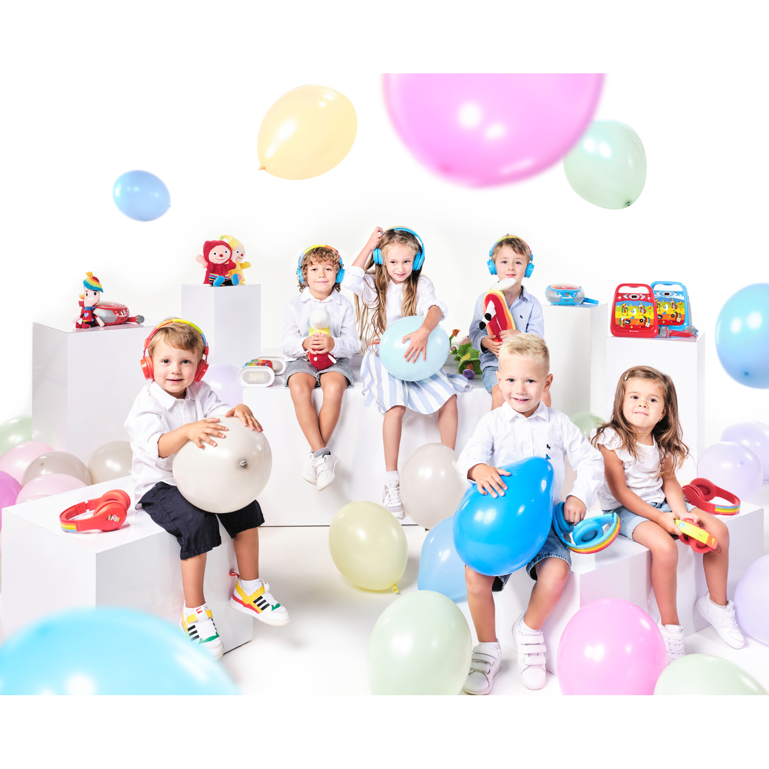 Bambini con cuffie seduti su cubi bianchi tengono palloncini e giocattoli.