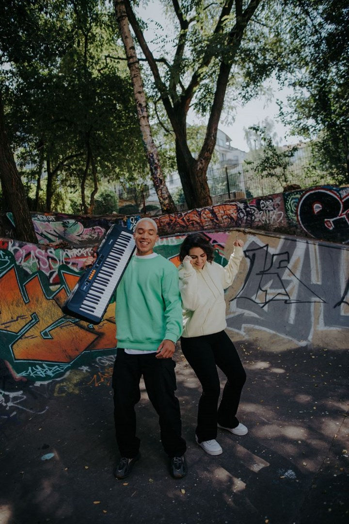 Een man met een keyboard en een vrouw dansend voor een graffiti muur.