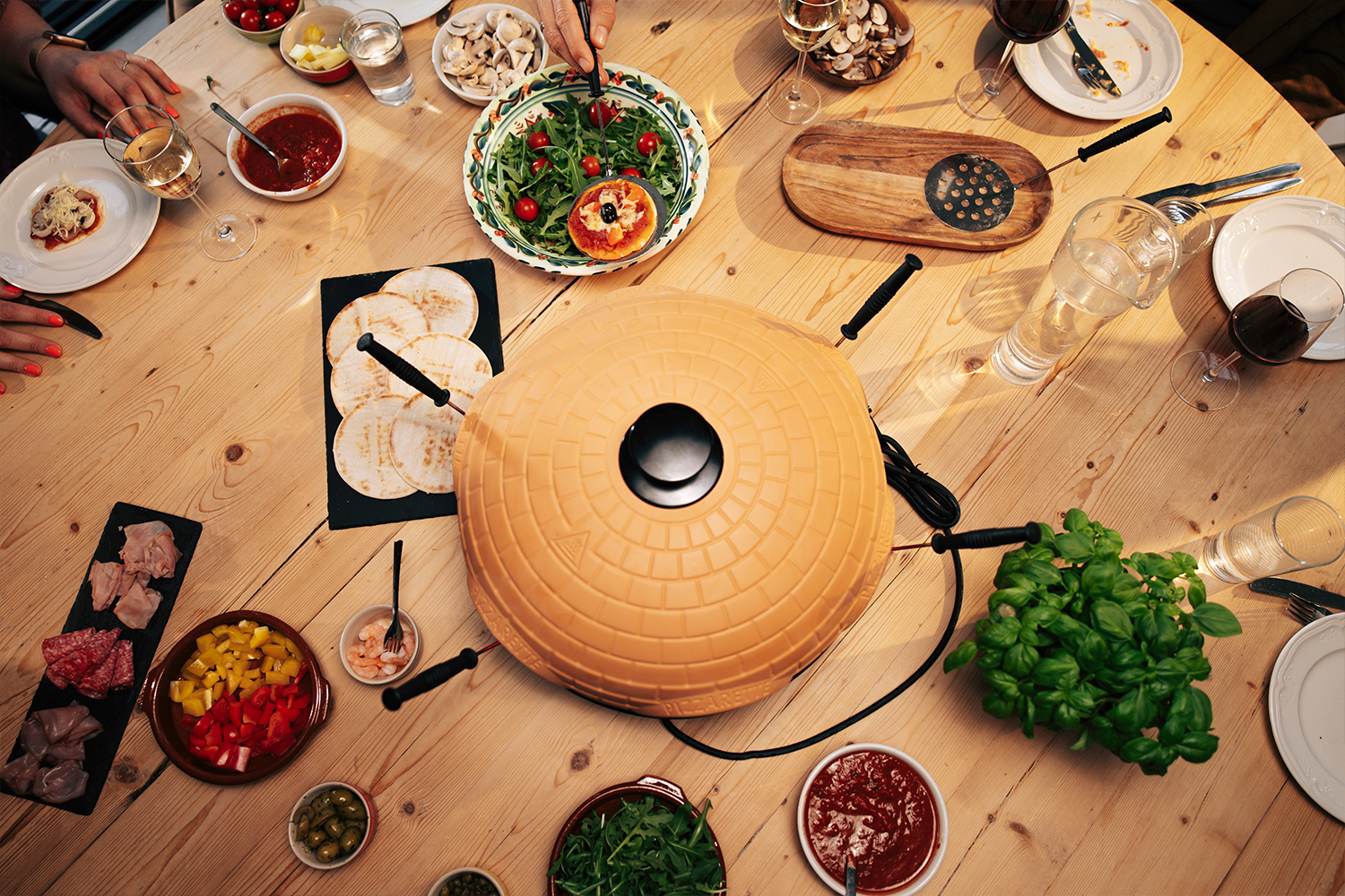 Een pizzarette met ingrediënten zoals deeg, saus, groenten en vlees op een houten tafel.
