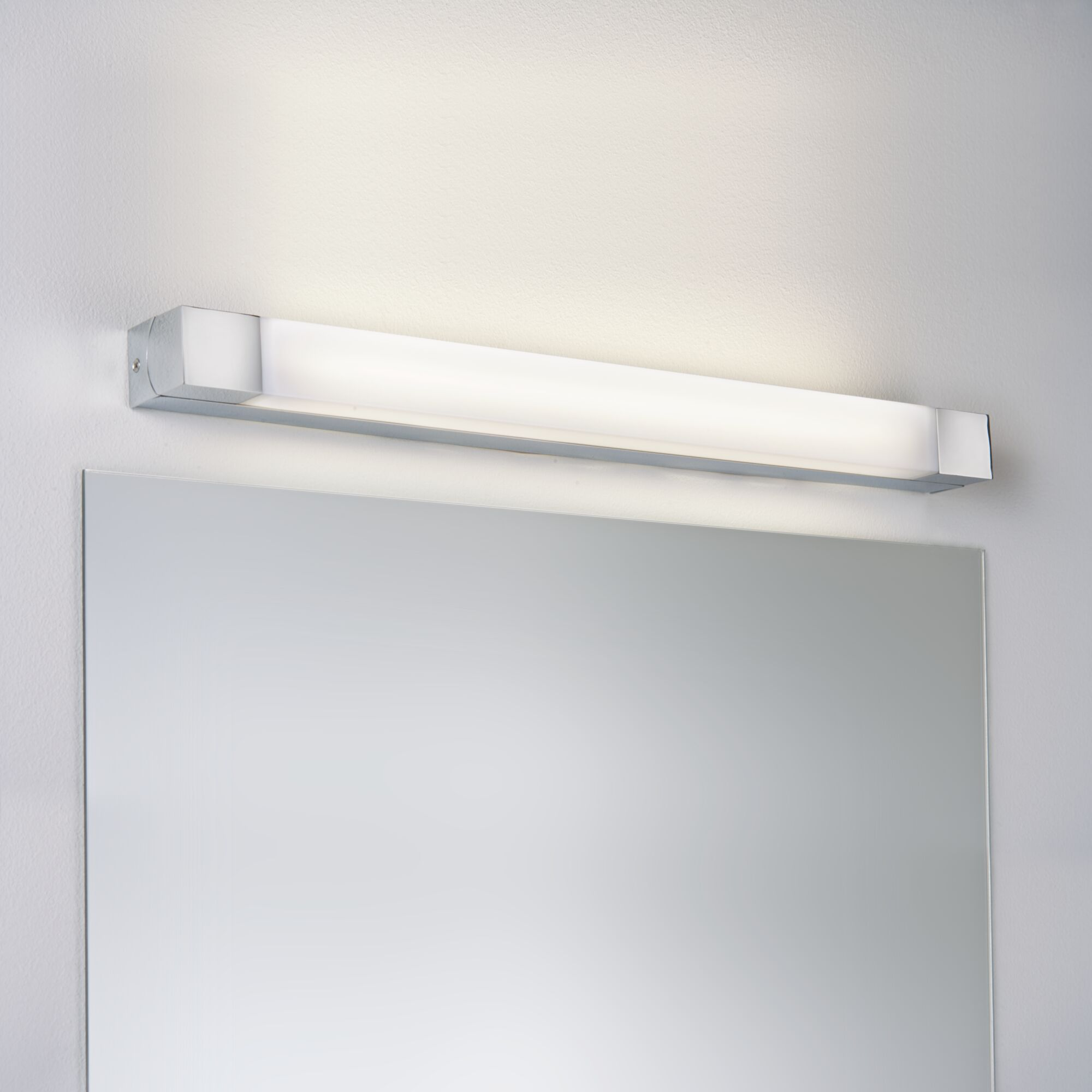 Ein langer, schmaler Spiegel mit einer darüber montierten Leuchte an einer weißen Wand.