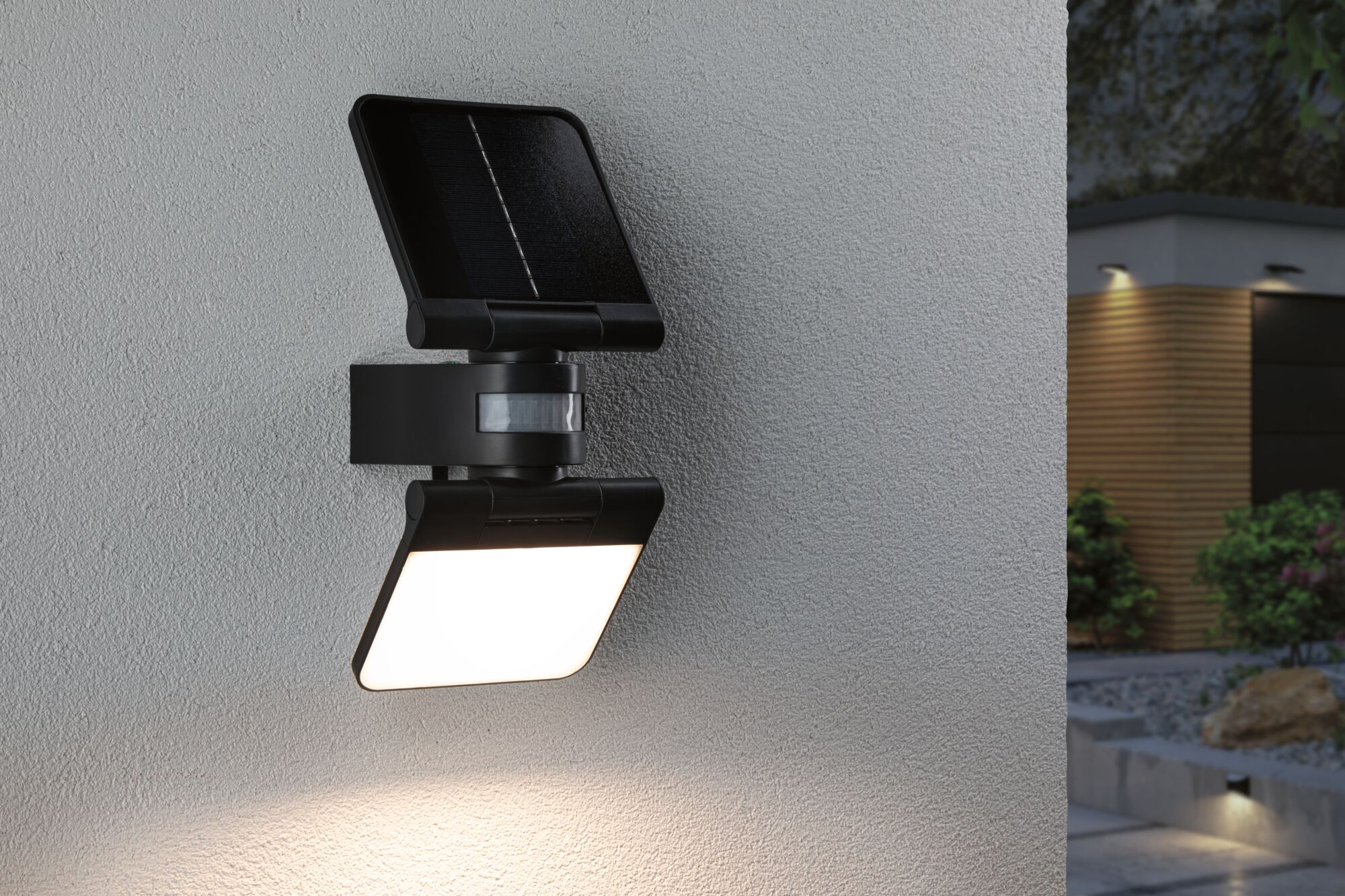 Czarna lampa solarna ścienna z czujnikiem ruchu oświetla teksturowaną ścianę.
