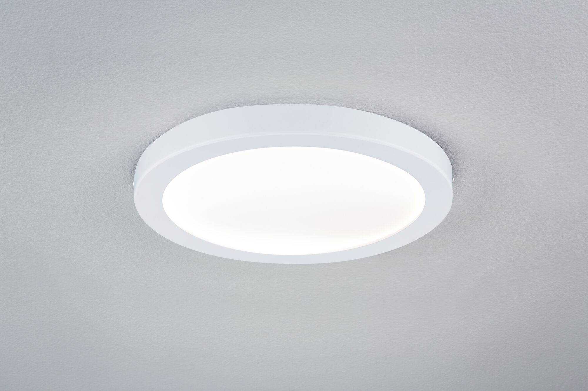 Una plafoniera bianca con diffusore rotondo e illuminato su un soffitto grigio.