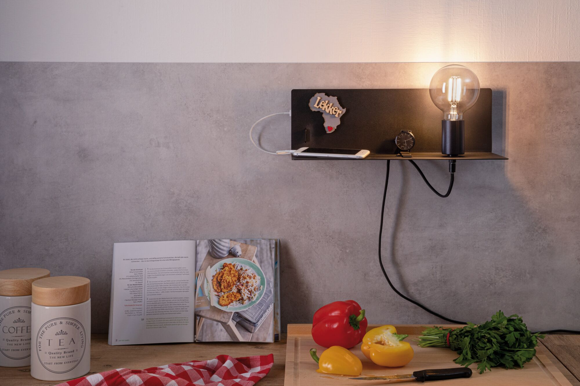 Ein Regal mit Lampe, Handy und Uhr. Daneben ein Kochbuch, Tee- und Kaffeedosen.