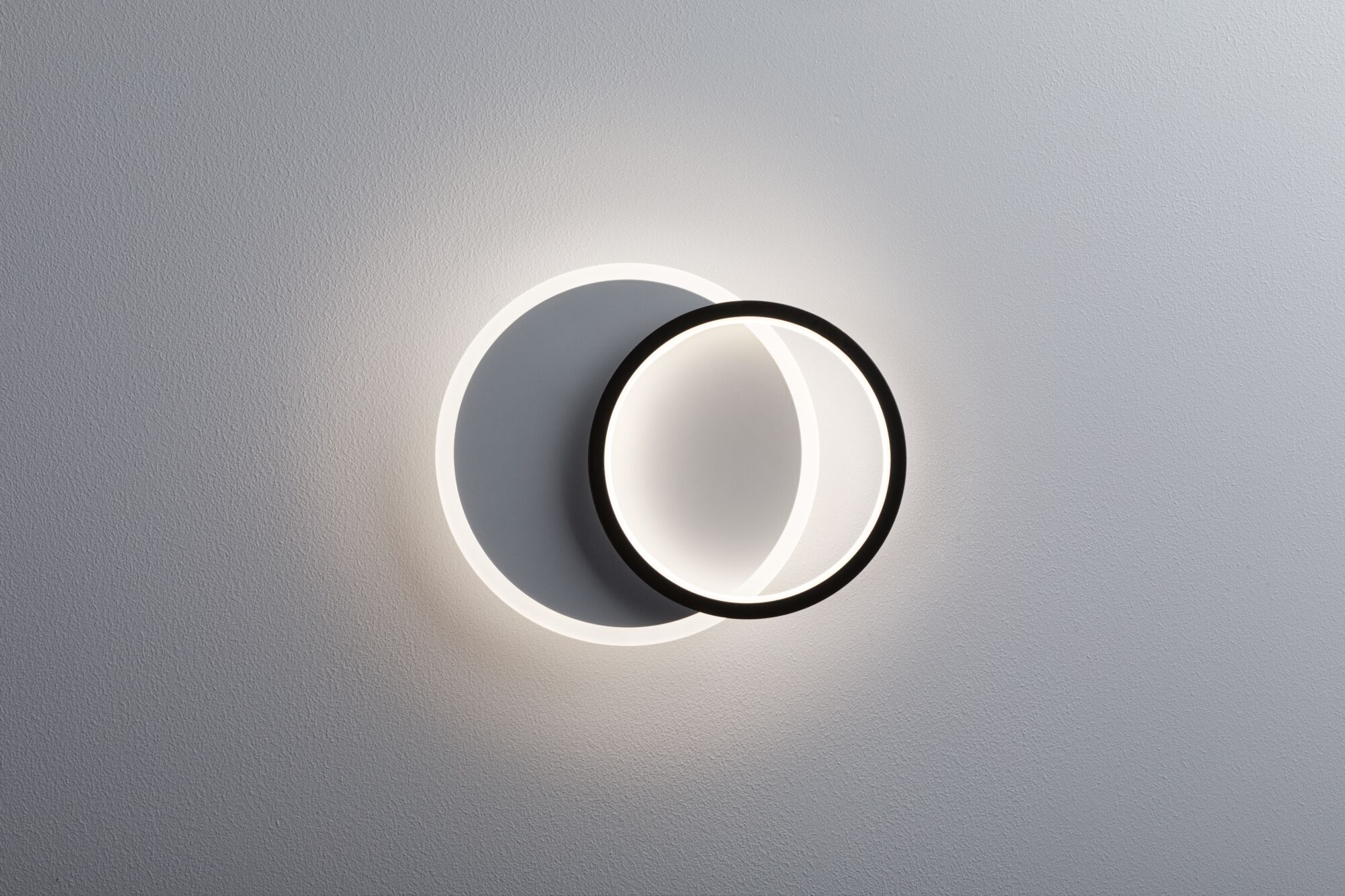 Nowoczesna lampa ścienna w dwóch nakładających się kołach z oświetleniem LED na szarej ścianie.