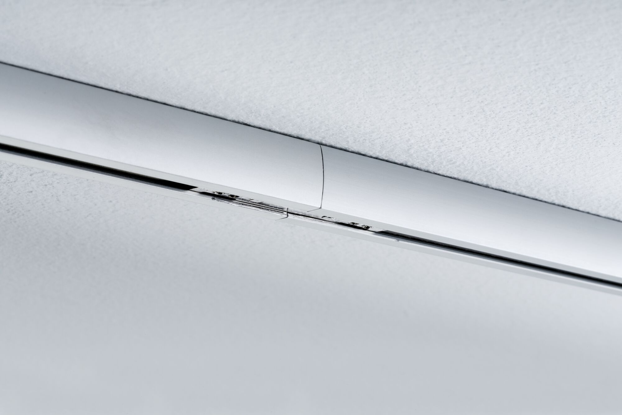 Eine metallische Leiste verläuft diagonal über eine weiße Decke.