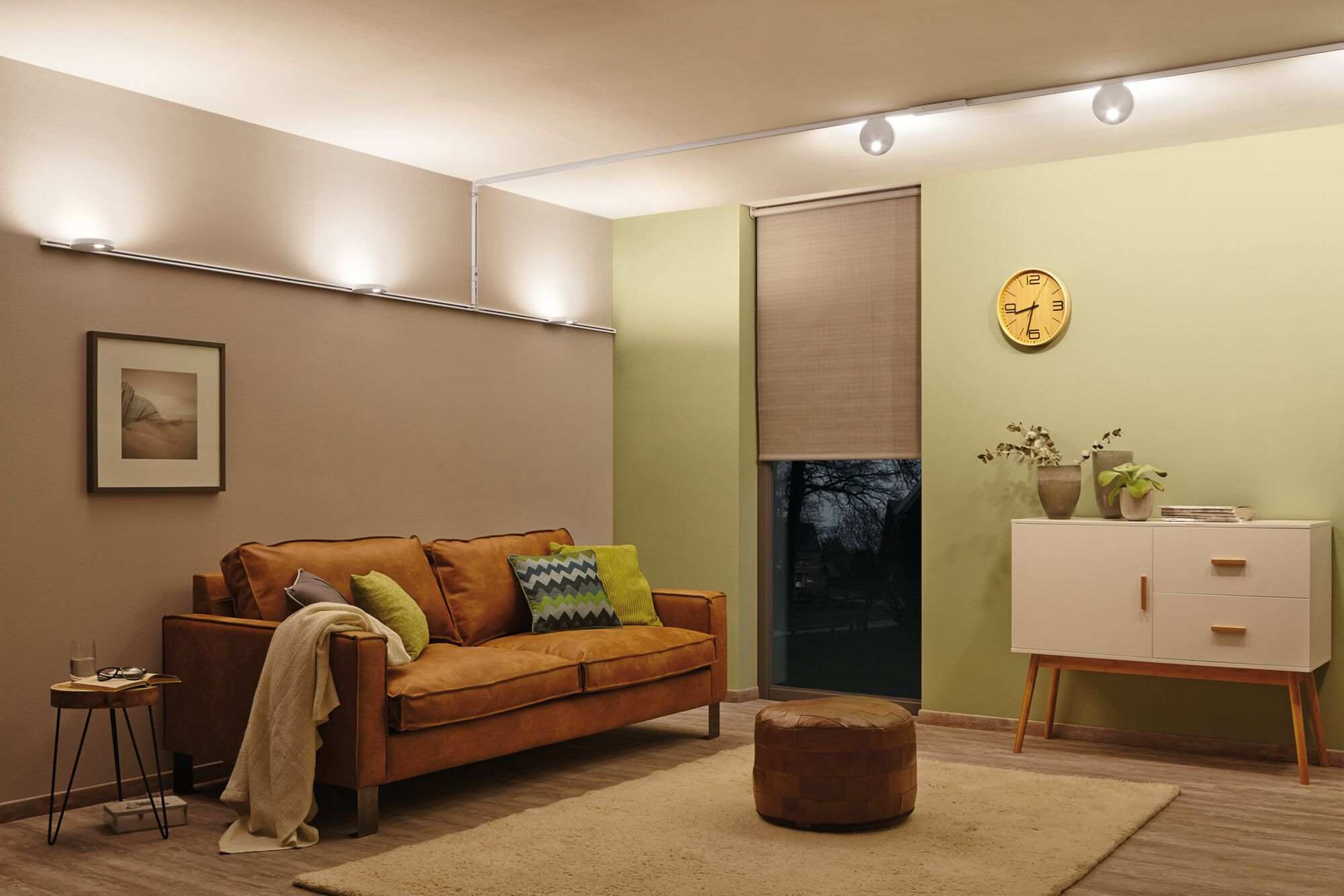 Ein Wohnzimmer mit braunem Sofa, Beistelltisch, Pouf und Kommode.