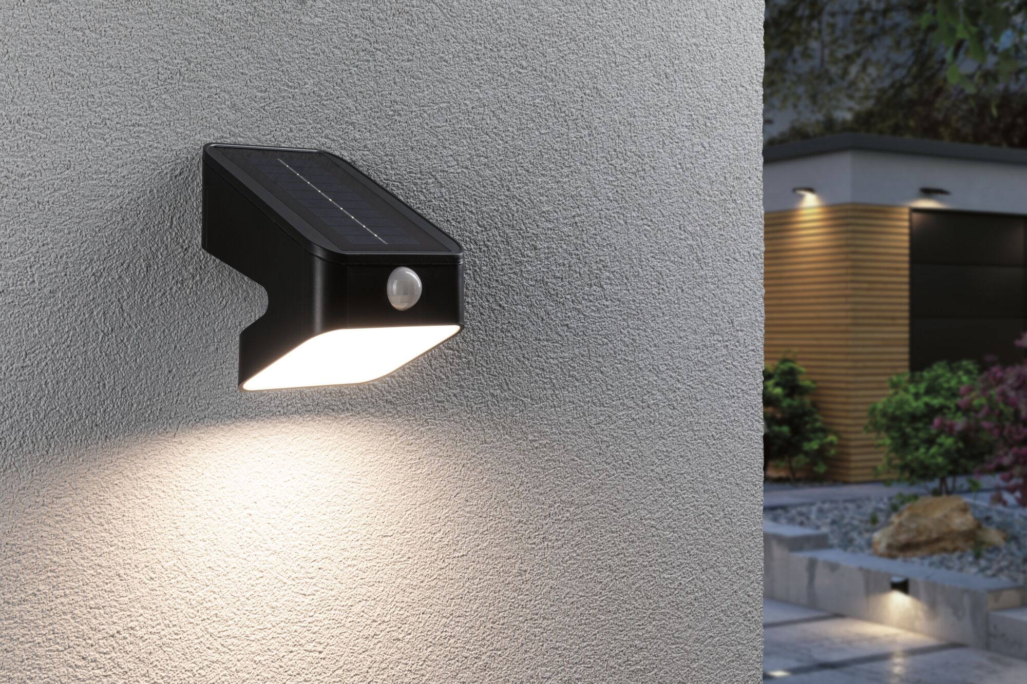Eine schwarze solarbetriebene Wandleuchte mit Bewegungsmelder beleuchtet eine graue Strukturwand.