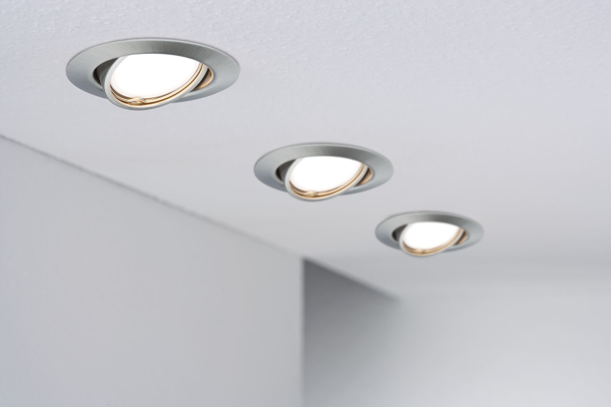 Drei Einbaustrahler mit silbernem Gehäuse und weißem Licht sind an einer Decke montiert.