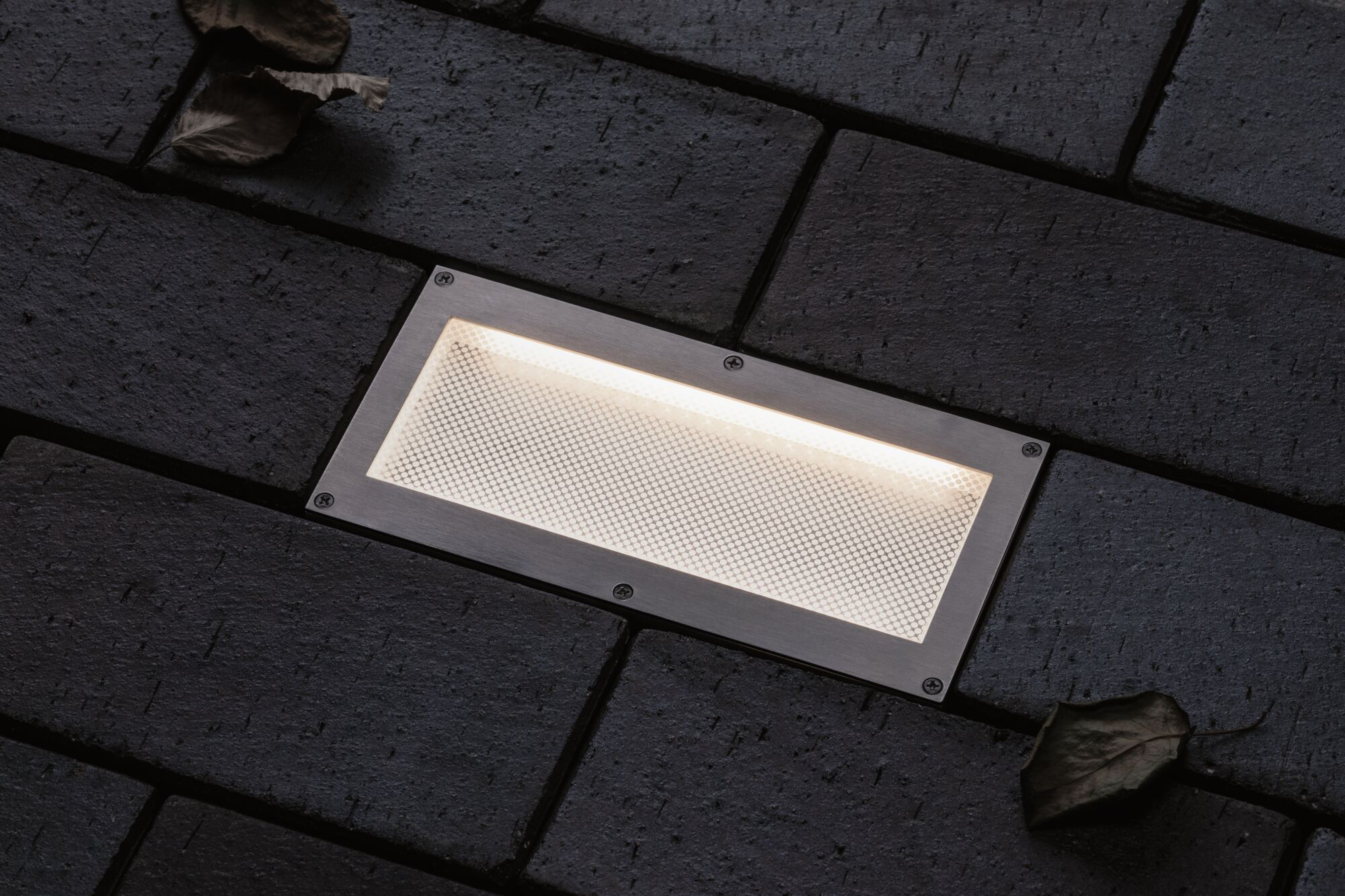 Prostokątna lampa wpuszczana z jasnym światłem na ciemnych cegłach.