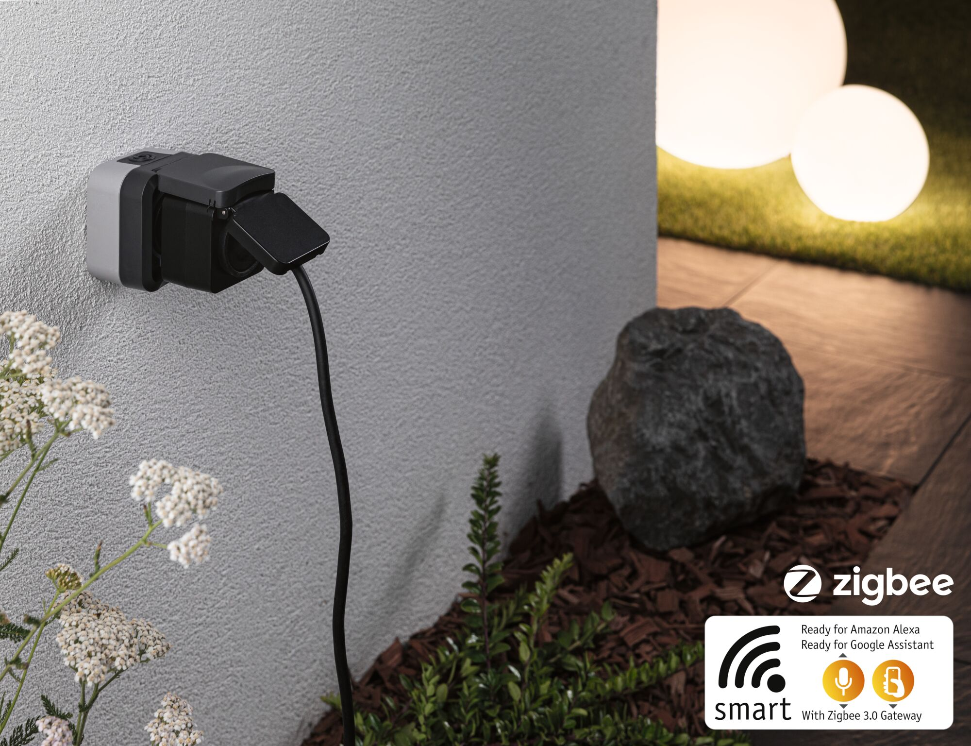Czarna wtyczka Zigbee na szarej ścianie, obok roślin i lamp kulistych.
