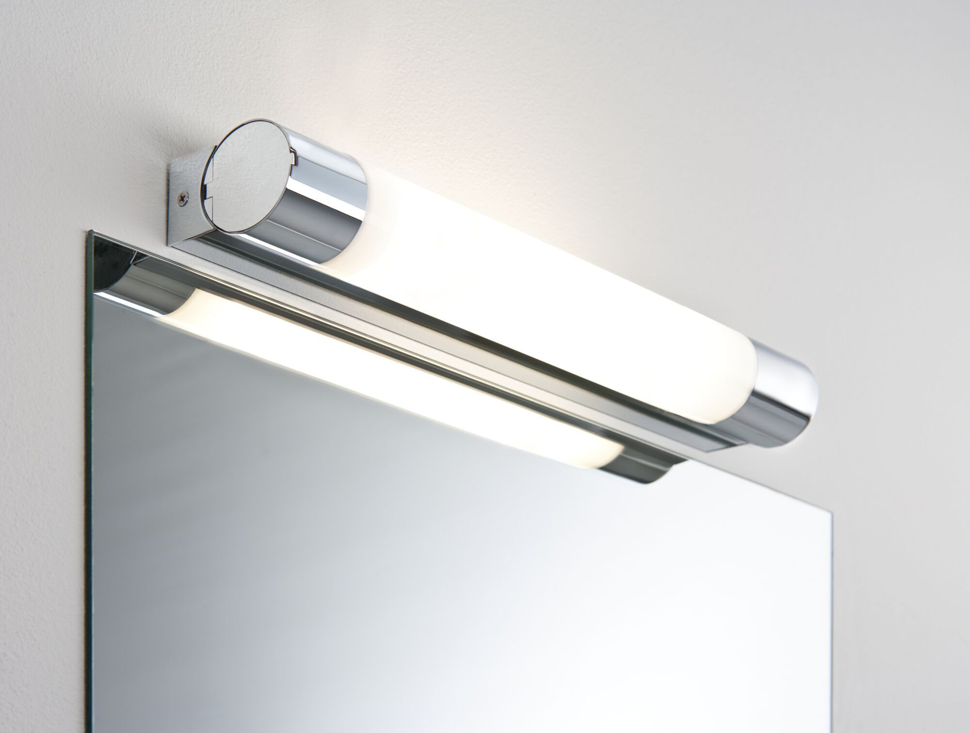Ein moderner Spiegel mit einer glatten, versilberten Oberfläche und einer Wandleuchte.
