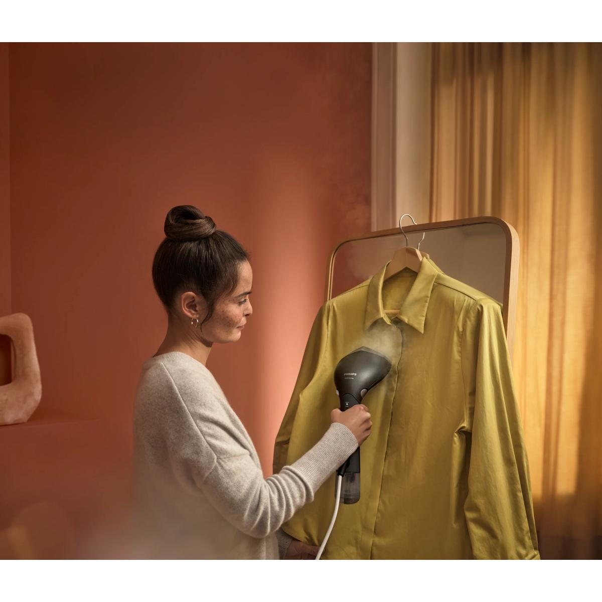 Donna che stira una camicia gialla con vaporizzatore portatile in una stanza elegante.