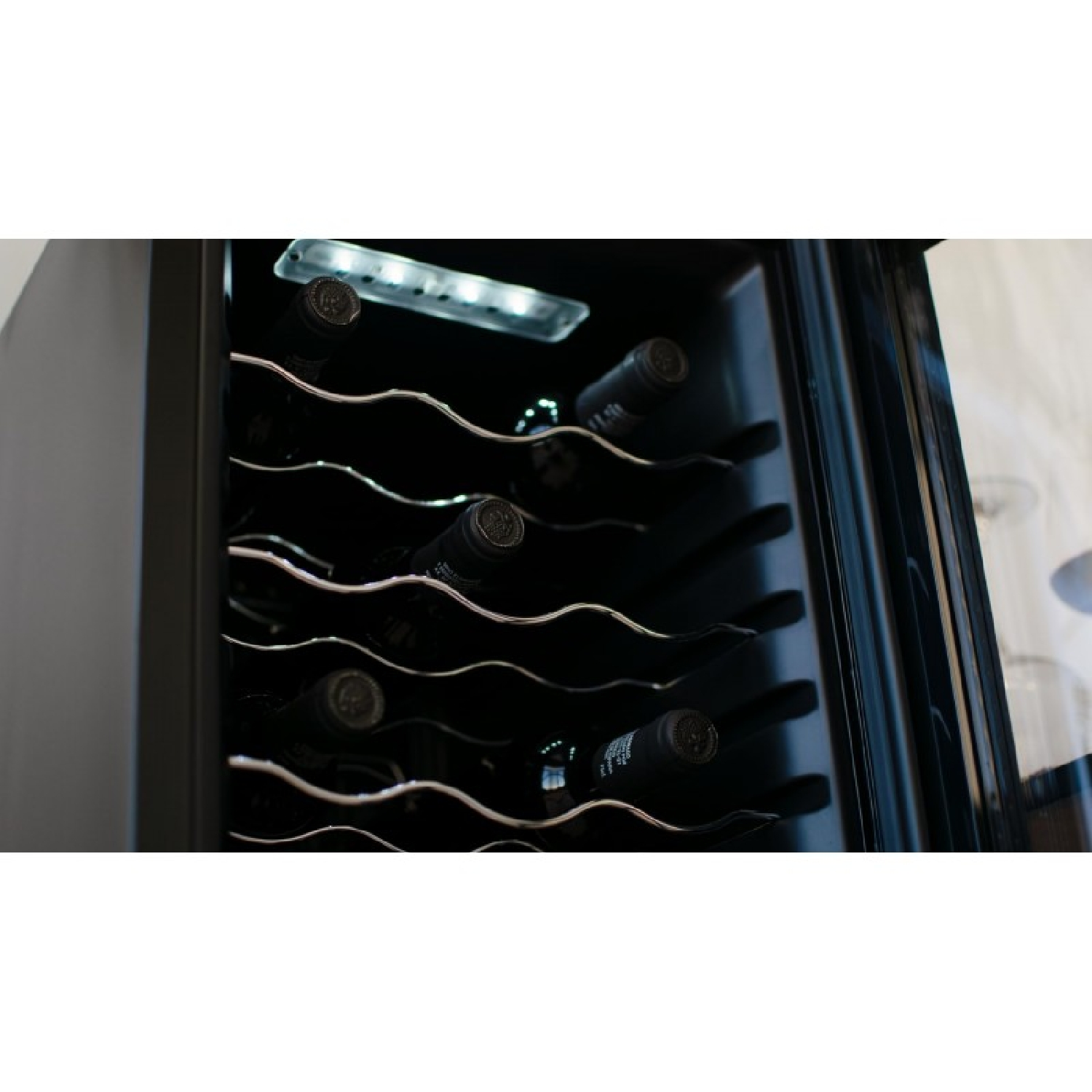 Cantinetta vino con più bottiglie su ripiani ondulati, illuminata.