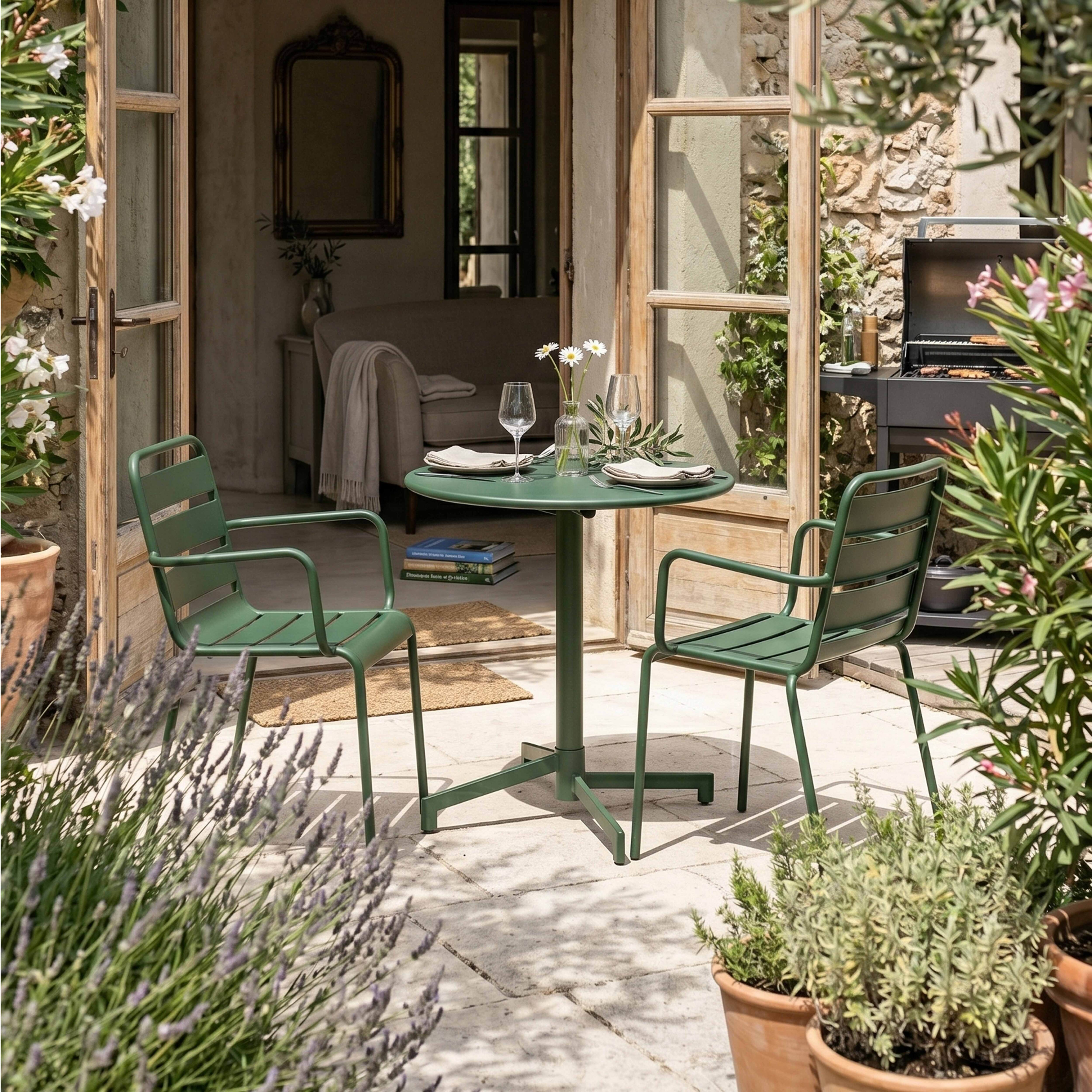 Ein grüner Gartentisch mit zwei Stühlen, Grill, Blumen und Pflanzen.