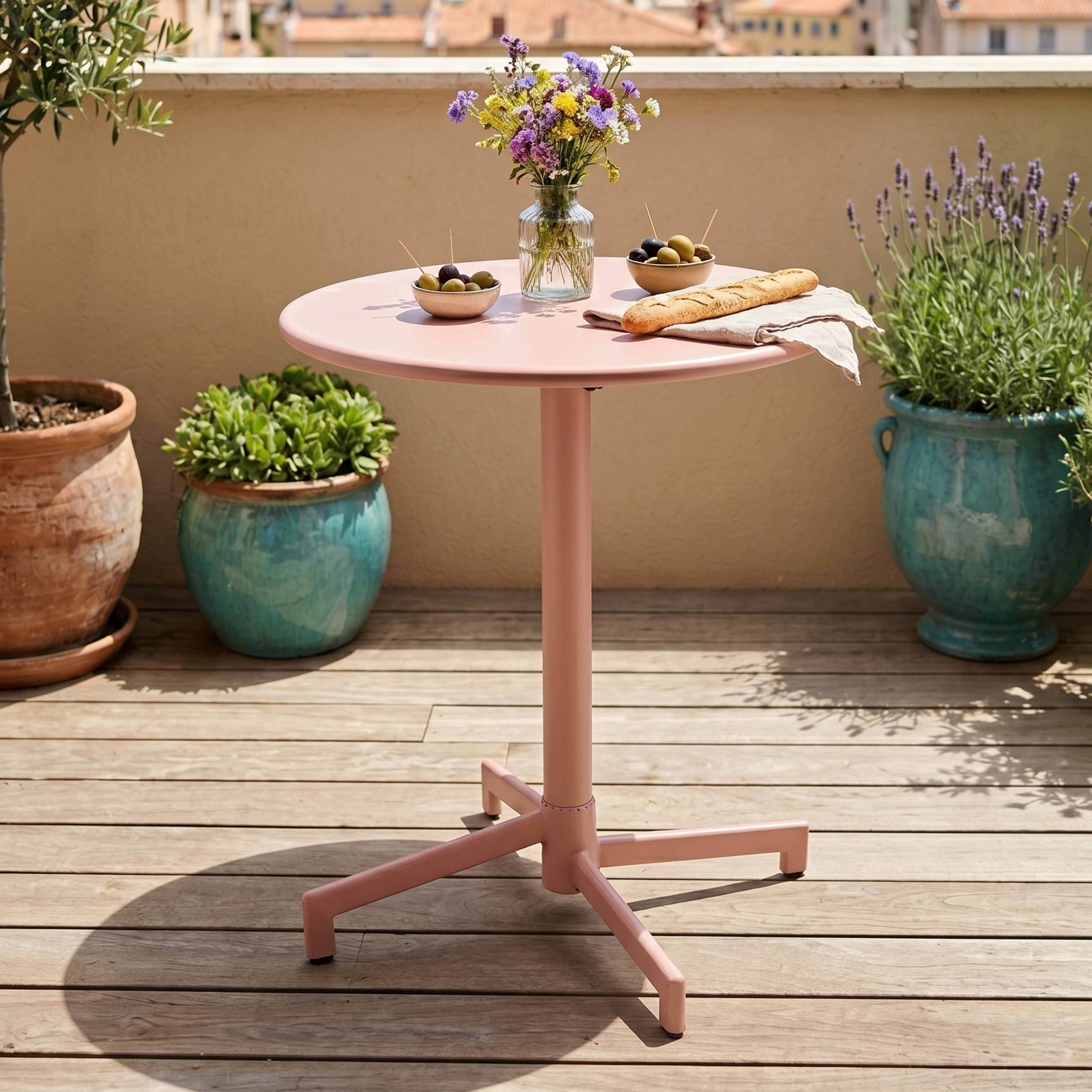 Ein runder, rosa Tisch mit Blumen, Brot und Oliven auf einer Holzterrasse.