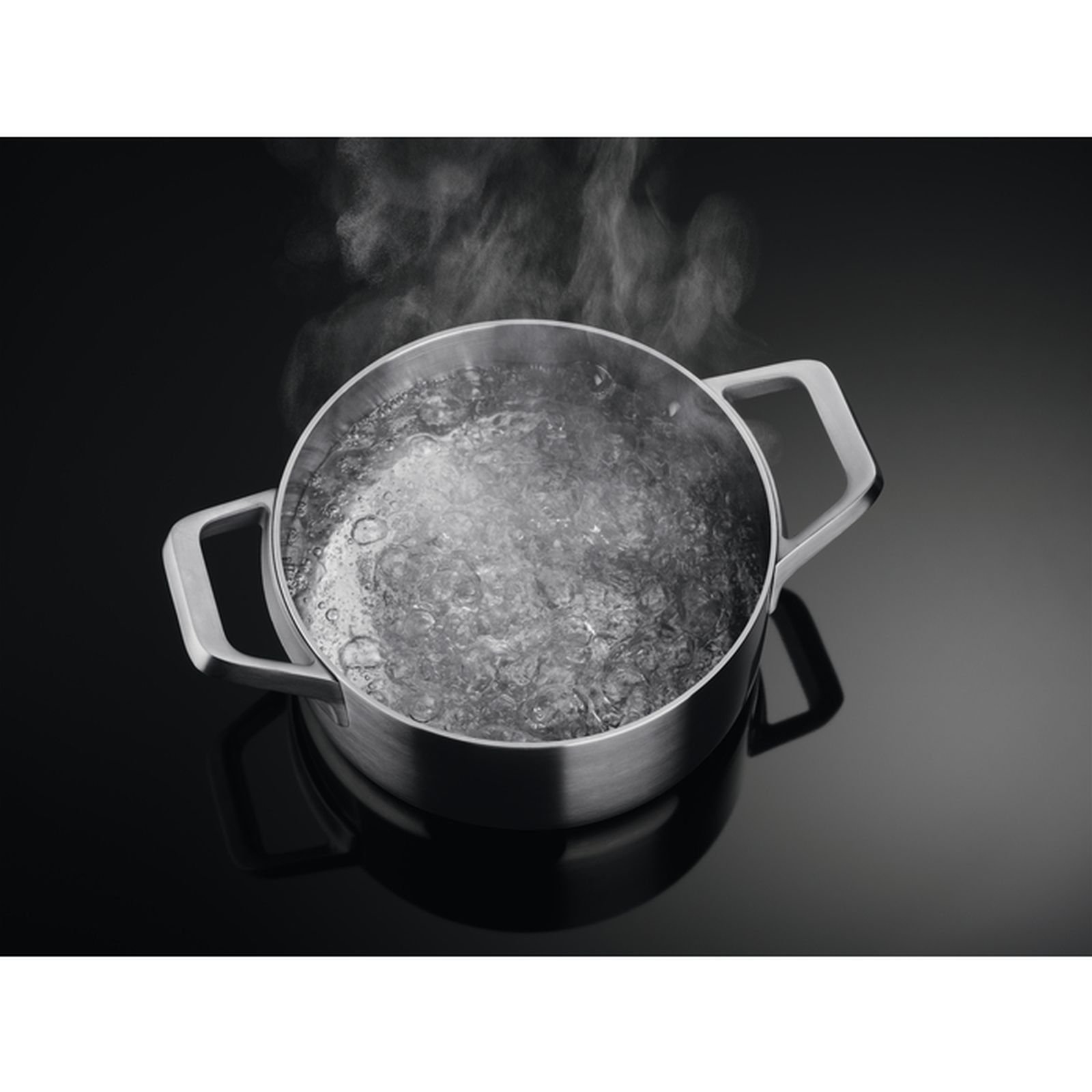 Una pentola argentata con acqua bollente su un piano cottura nero. Il vapore sale.