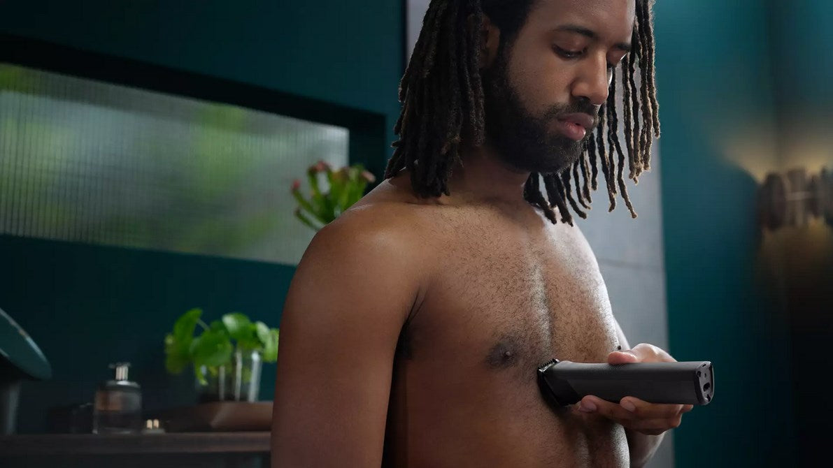 Hombre con rastas usando recortadora corporal en el pecho en baño.