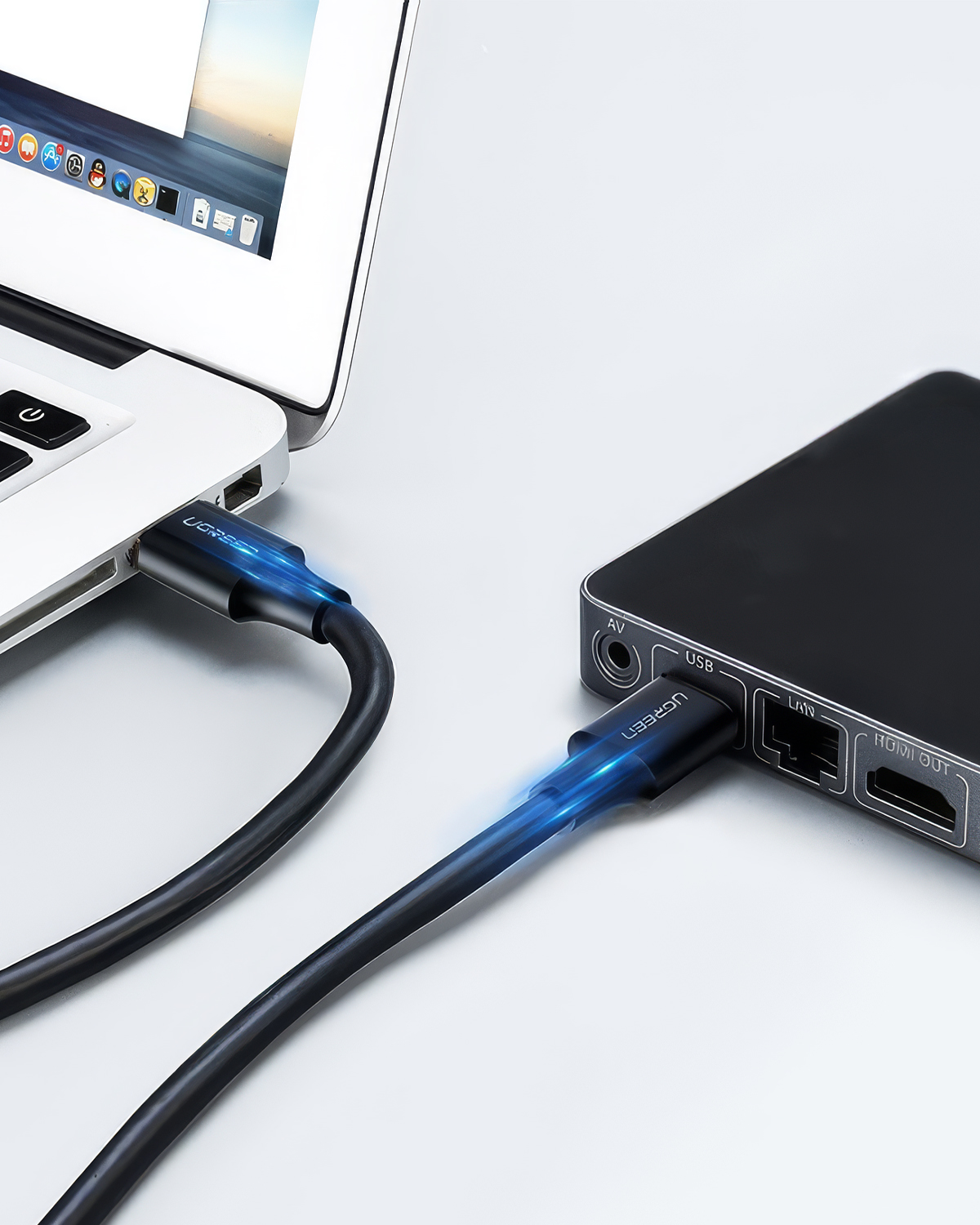 Siyah bir USB-C kablosu, dizüstü bilgisayarı bir cihaza bağlıyor, konektörde mavi parlıyor.