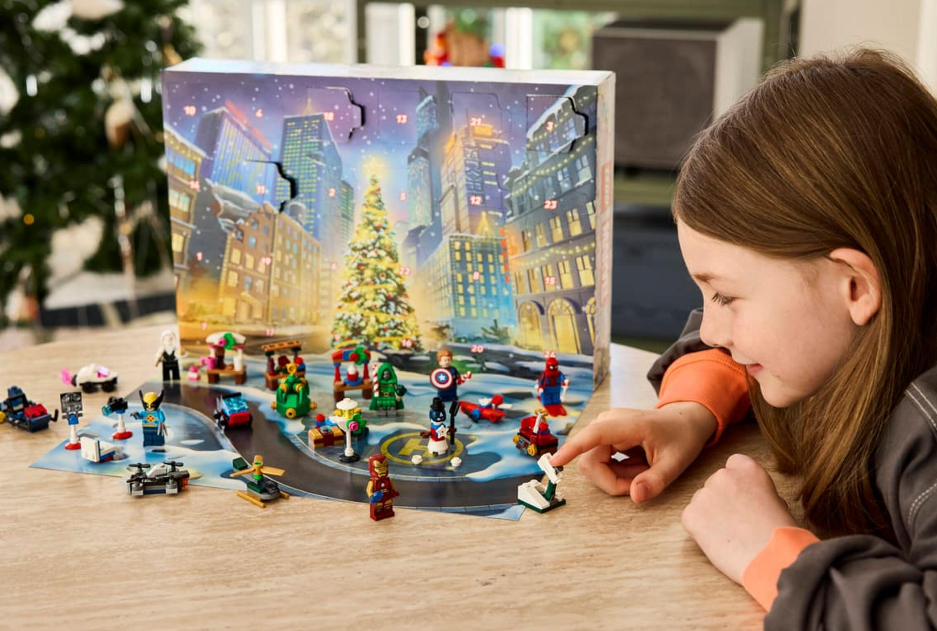 Una niña abre un calendario de adviento de superhéroes frente a un paisaje urbano iluminado.