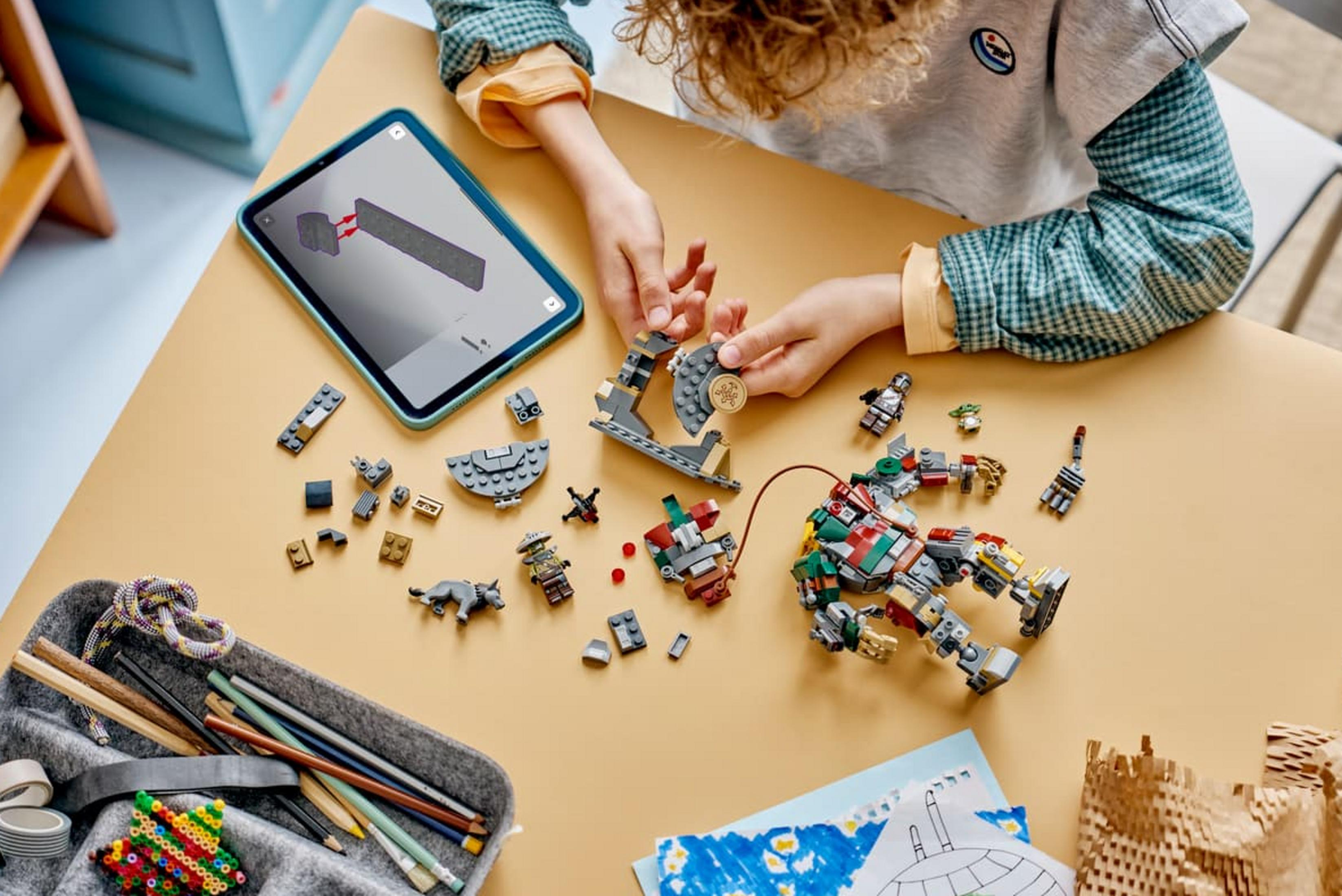 Bir çocuk Lego tuğlalarıyla inşa ediyor, talimatlar tablet üzerinde görünüyor.