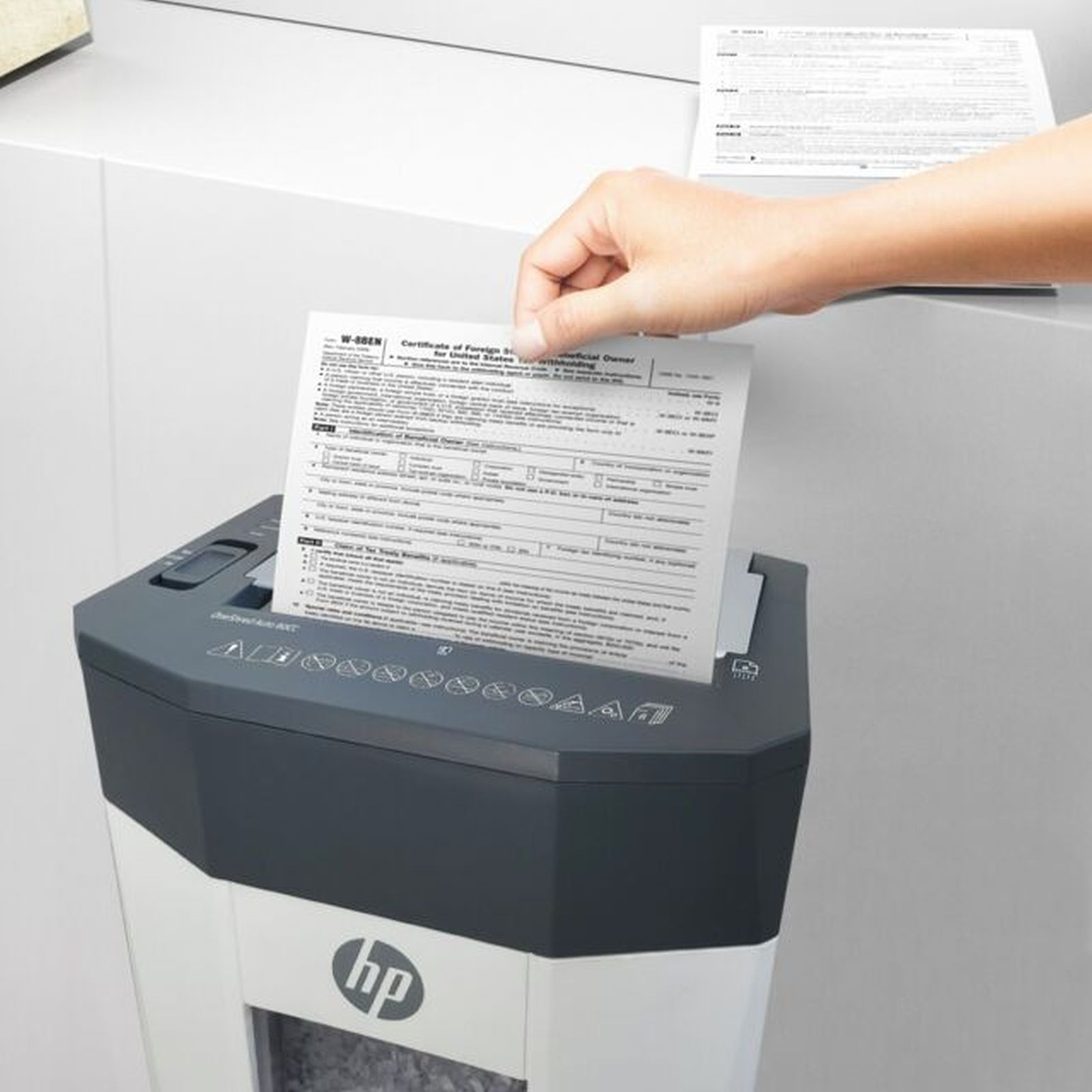 Una mano inserisce un modulo W-8BEN in un distruggi documenti.