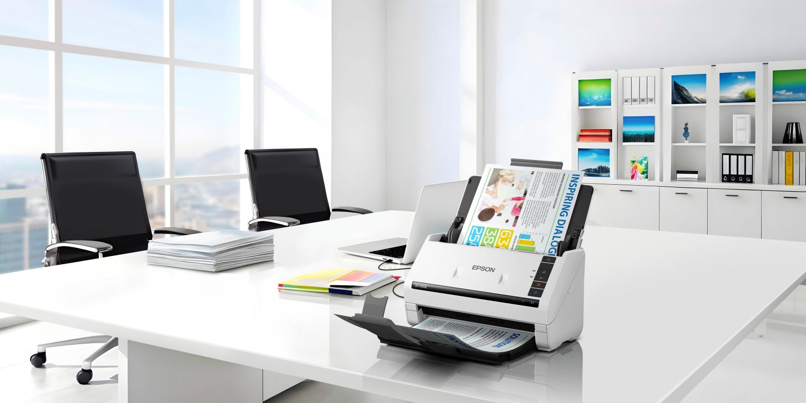 Un ufficio moderno con scrivania, scanner, laptop, carte e sedie vicino a una finestra.