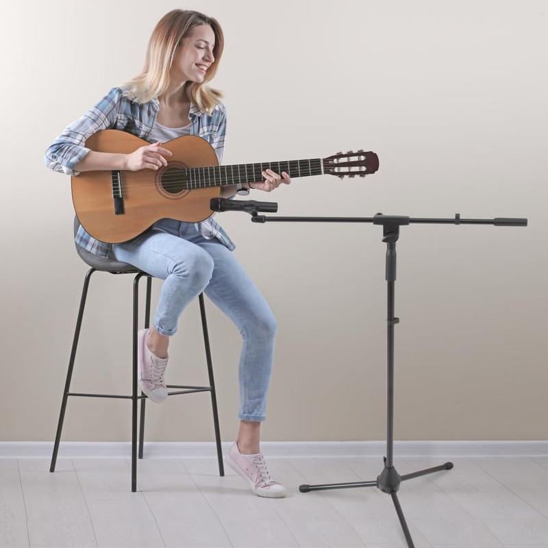 Eine Frau sitzt auf einem Hocker und spielt Gitarre vor einem Mikrofonständer.