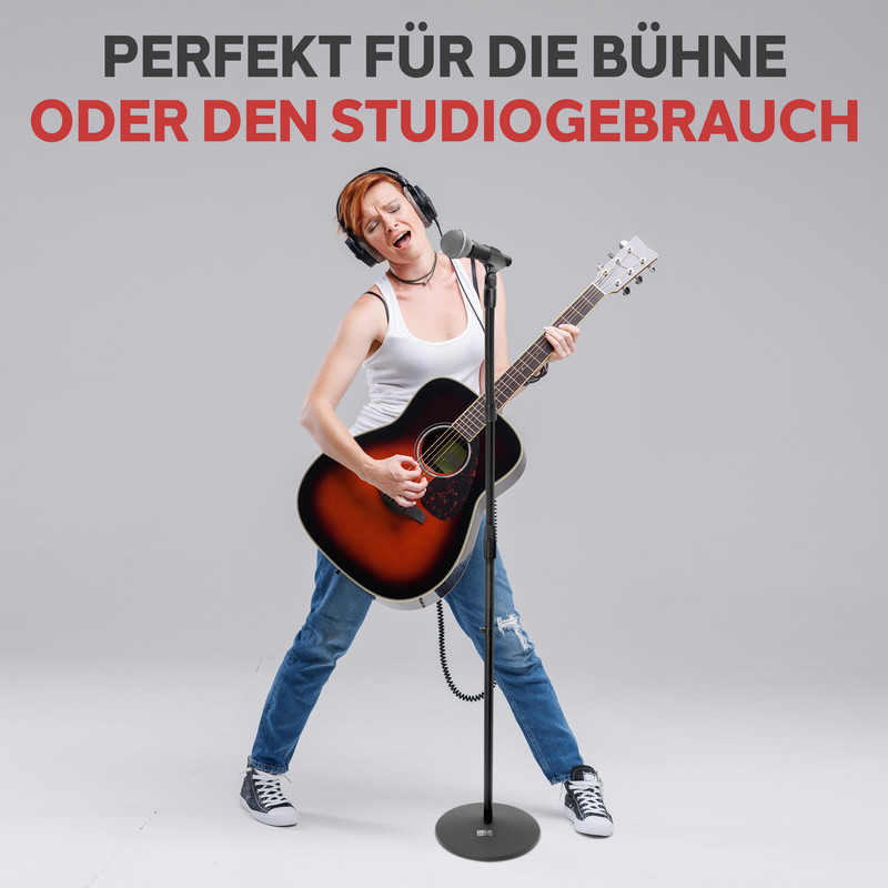 Frau mit Kopfhörern spielt Gitarre und singt in ein Mikrofon.