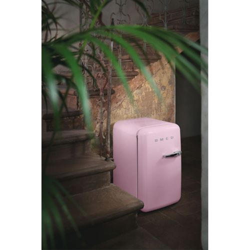 Un pequeño frigorífico rosa Smeg junto a una escalera de madera con barandilla ornamentada.