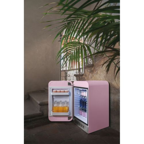 Un mininevera rosa retro está abierto, mostrando bebidas y comida. Está al aire libre.